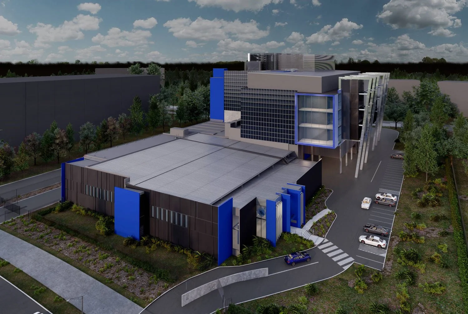 A modern multi-story building with glass and blue accents, surrounded by parking lots with several cars and lush green trees under a partly cloudy sky.