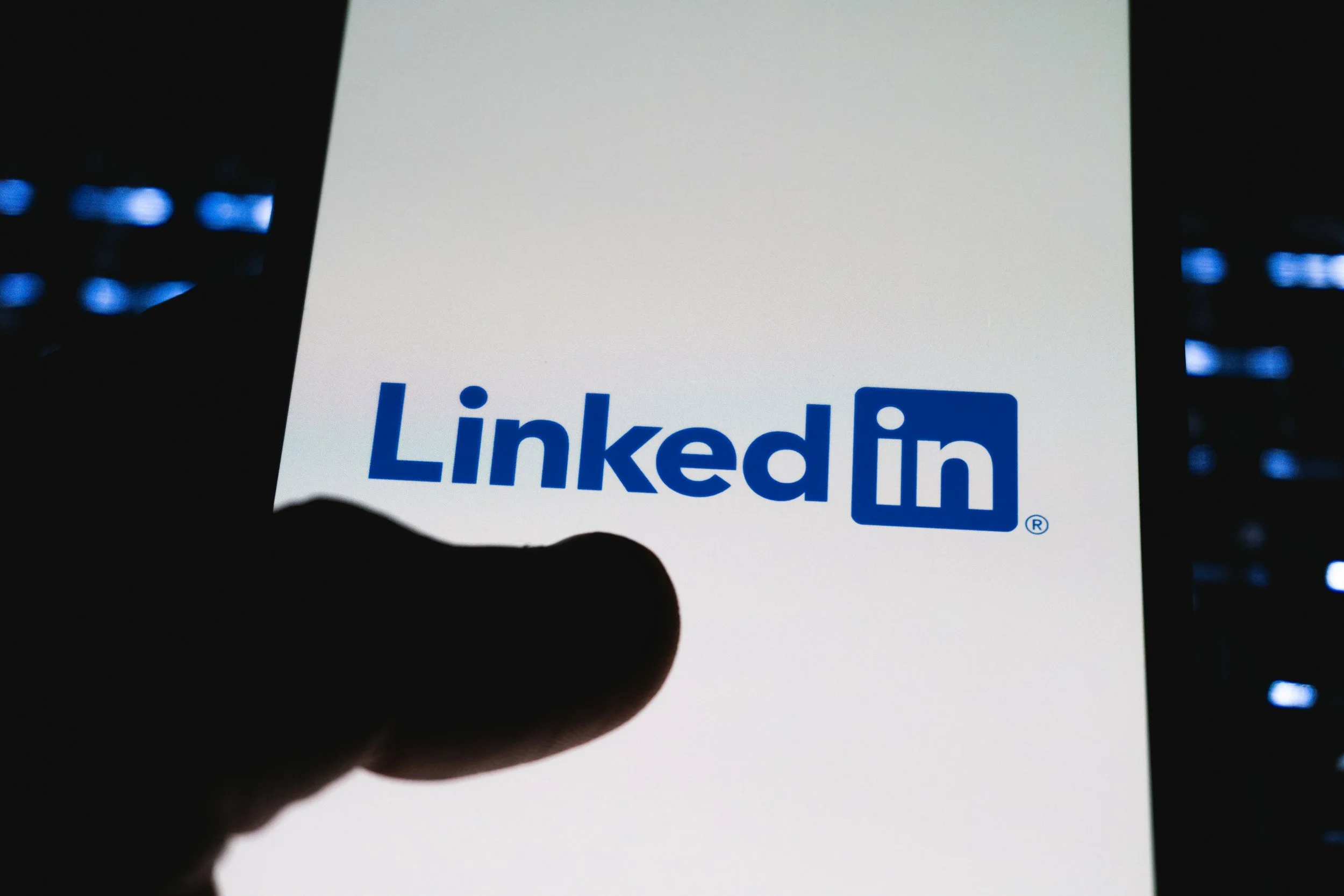 A person holding a smartphone displaying the LinkedIn logo on the screen.