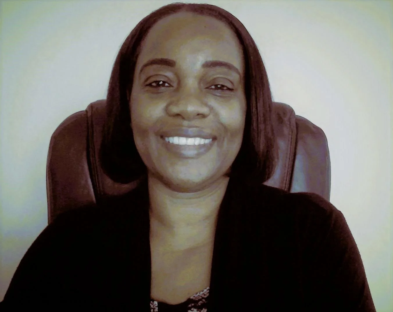 A woman smiling and sitting in a leather chair in front of a plain wall.