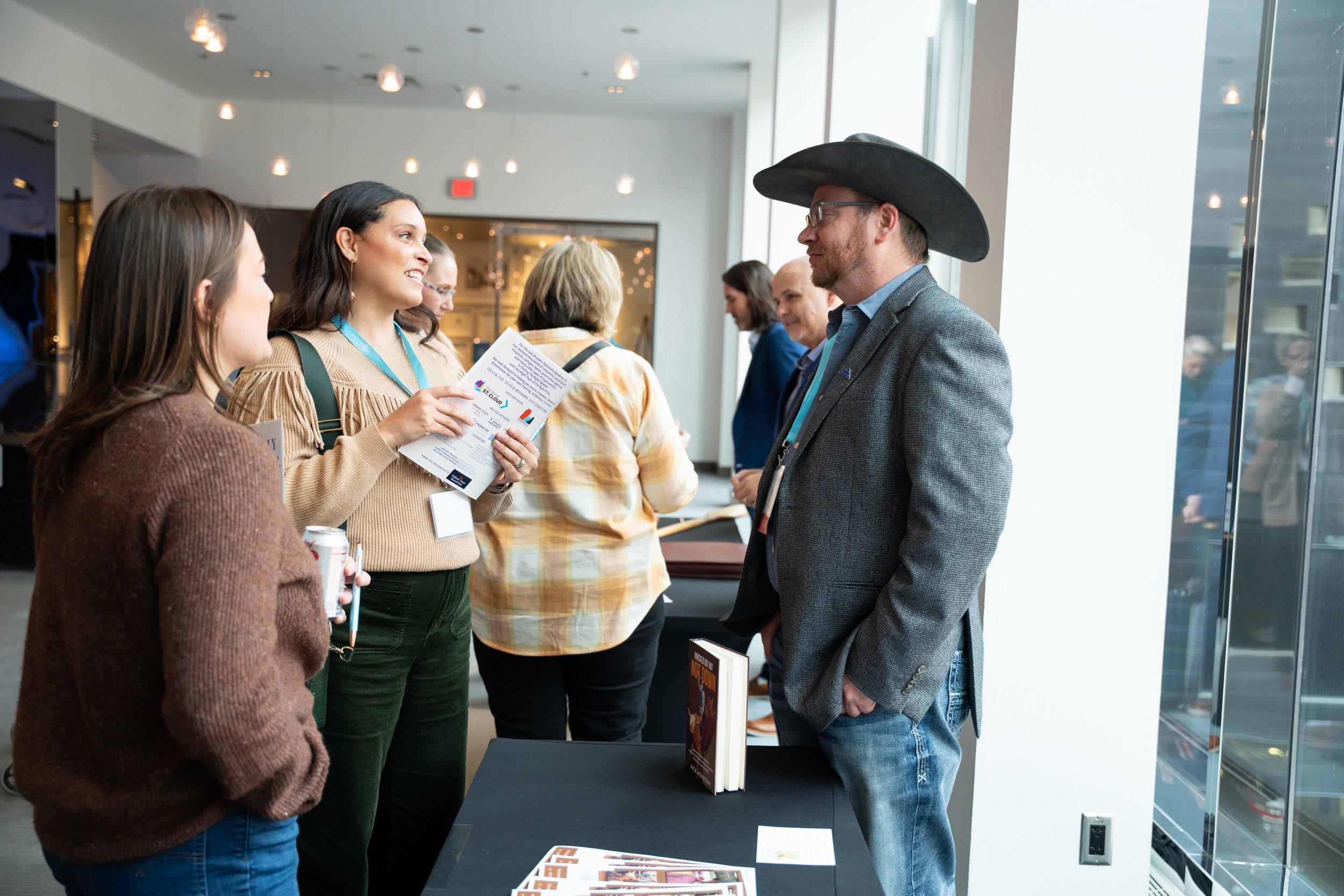 Group of four people conversing at a professional event, with a man wearing a cowboy hat and a woman holding a pamphlet.