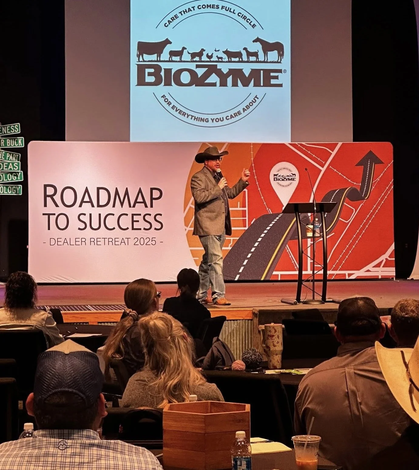 A man in a cowboy hat and blazer giving a presentation on a stage at a conference titled 'Roadmap to Success - Dealer Retreat 2025'. Audience members are seated watching the presentation.