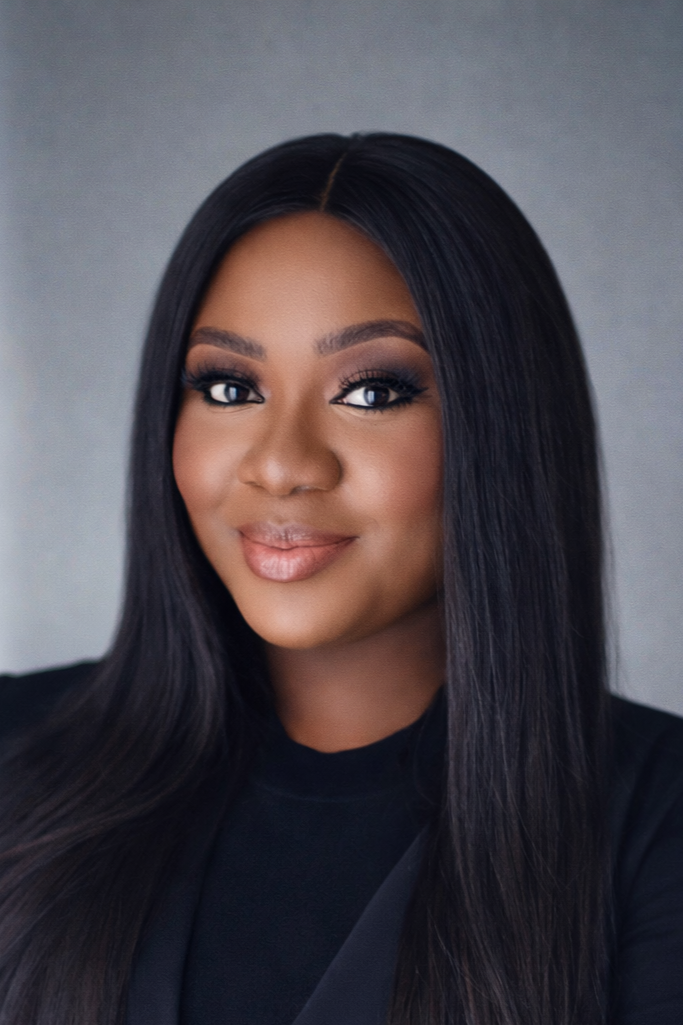 Portrait of a woman with long black hair, makeup, and a black top, smiling softly against a gray background.