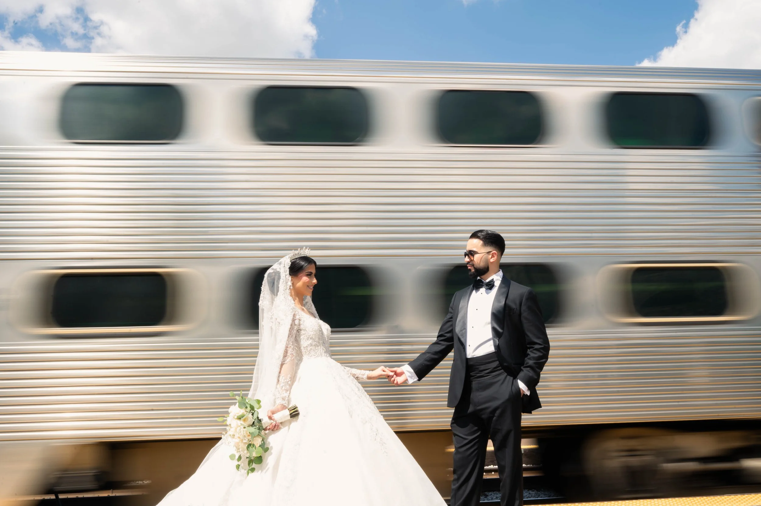 Bride and groom in wedding attire holding hands in front of a moving train