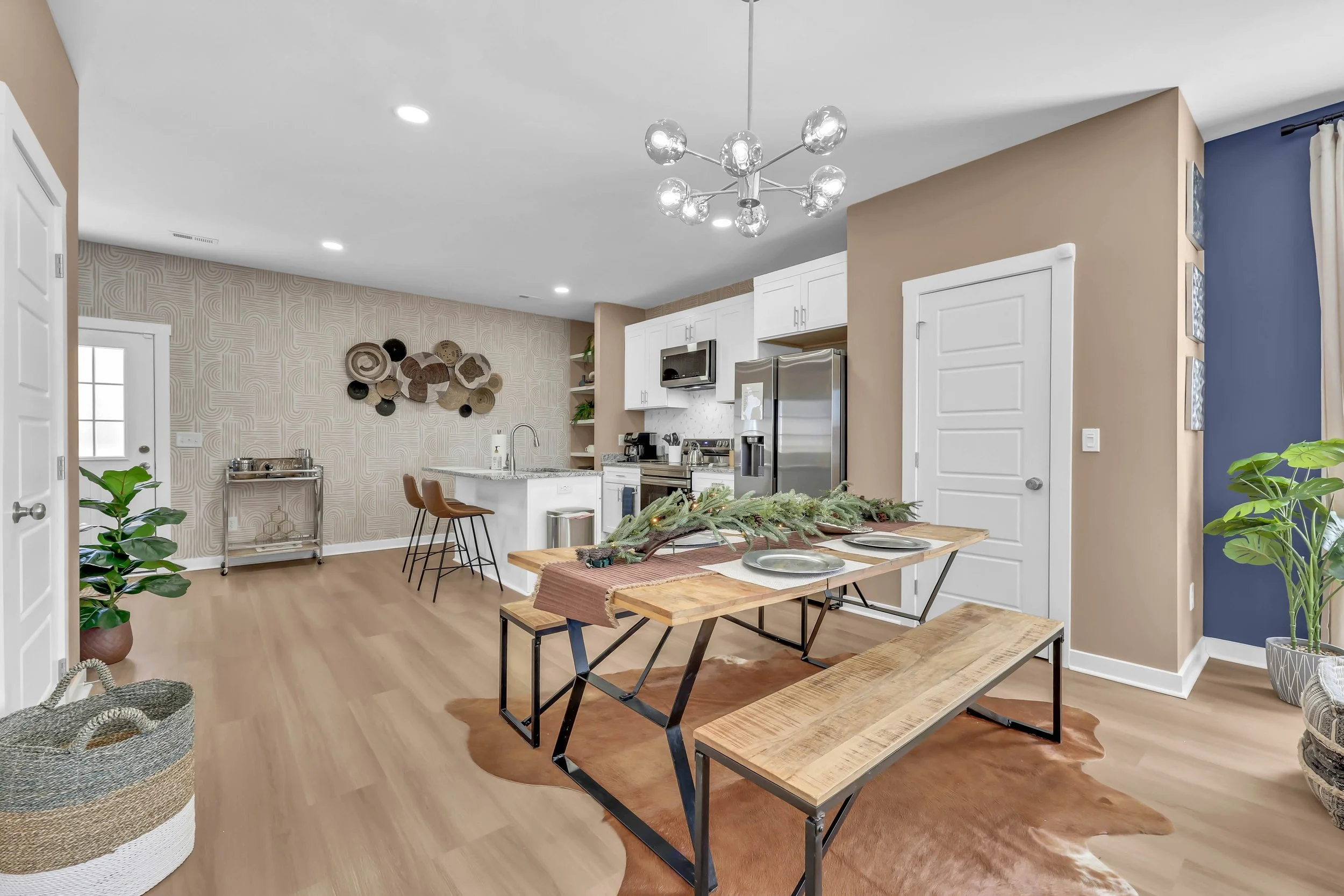 Open-concept kitchen and dining area with hardwood floors, beige and blue accent walls, modern chandelier, and a dining table with bench seating and a centerpiece of greenery.