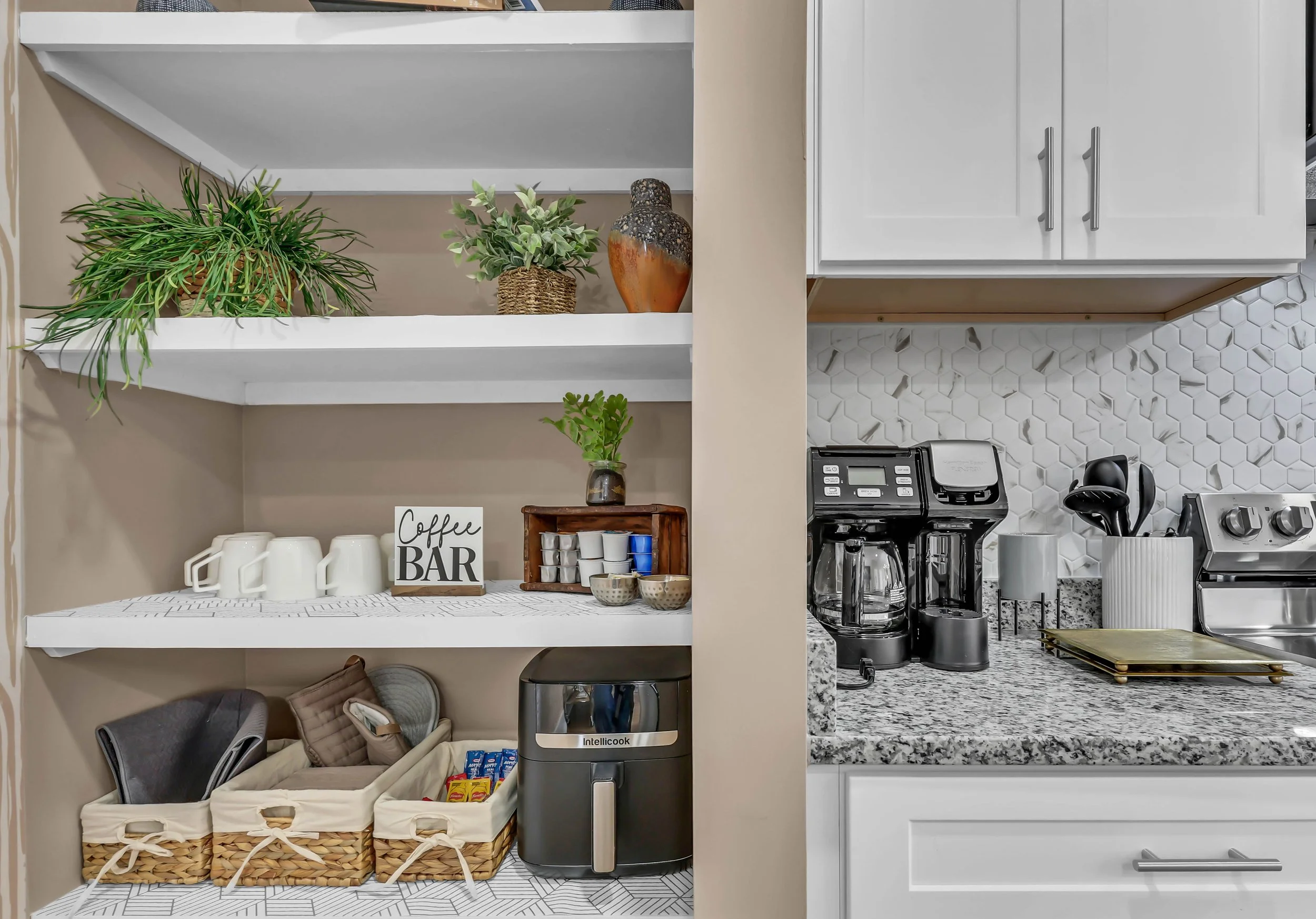 Kitchen corner with open shelves displaying cups, plants, decorative items, and a coffee station next to a stove with a coffee maker, toaster, and utensils.