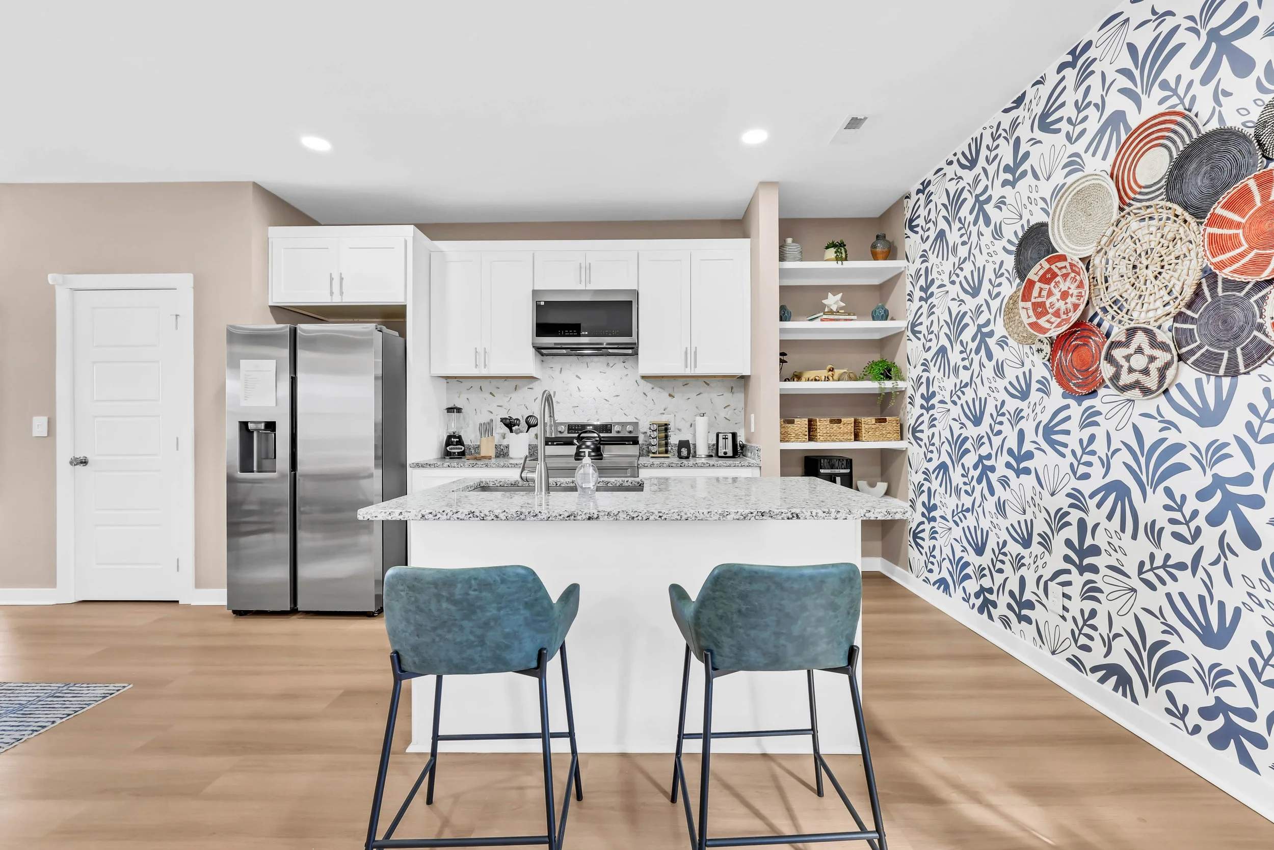 Modern kitchen with white cabinets, gray countertops, stainless steel refrigerator, and a blue and white patterned accent wall with decorative plates.