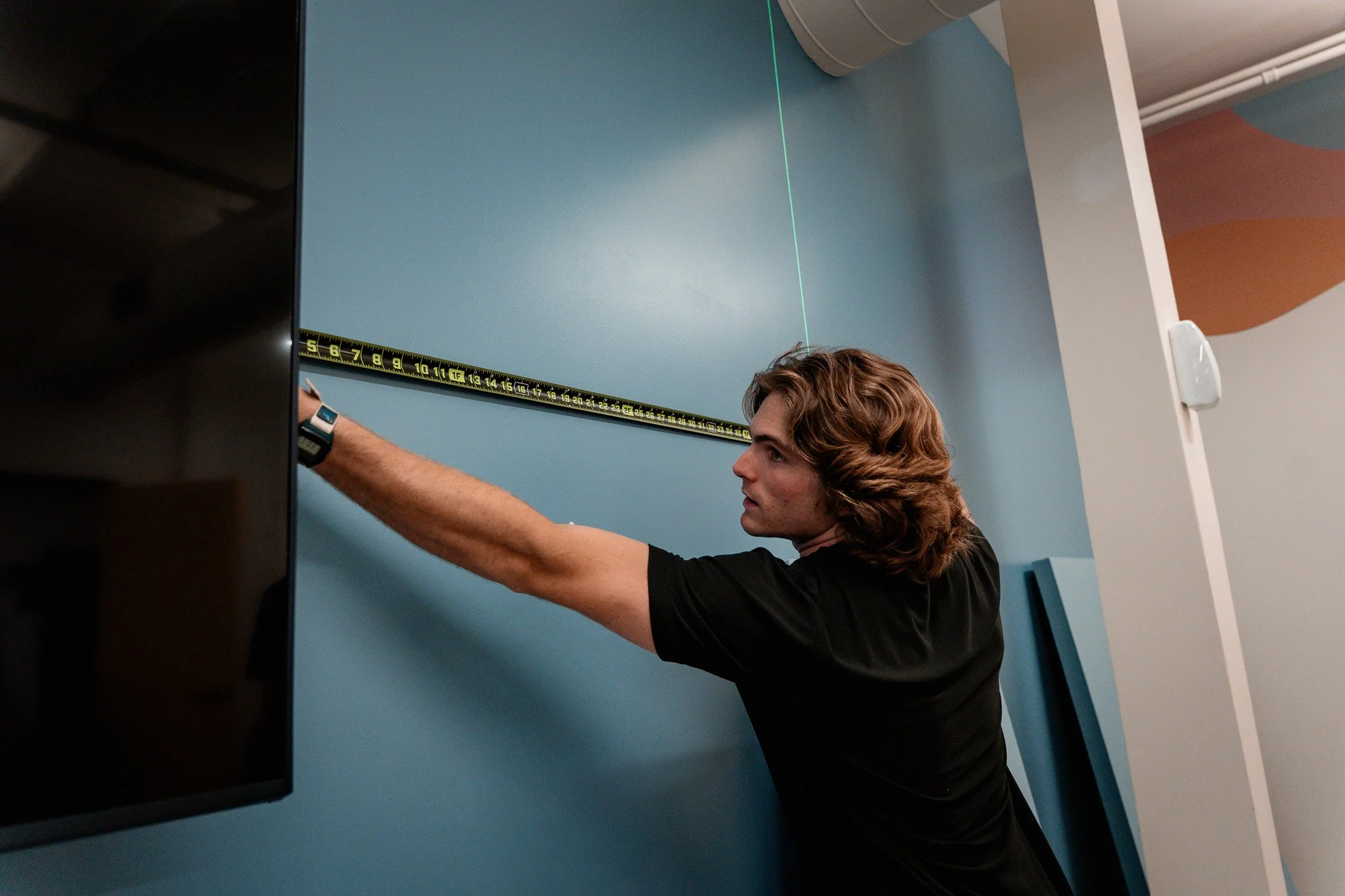 Young man measuring wall height with a tape measure in a modern room.
