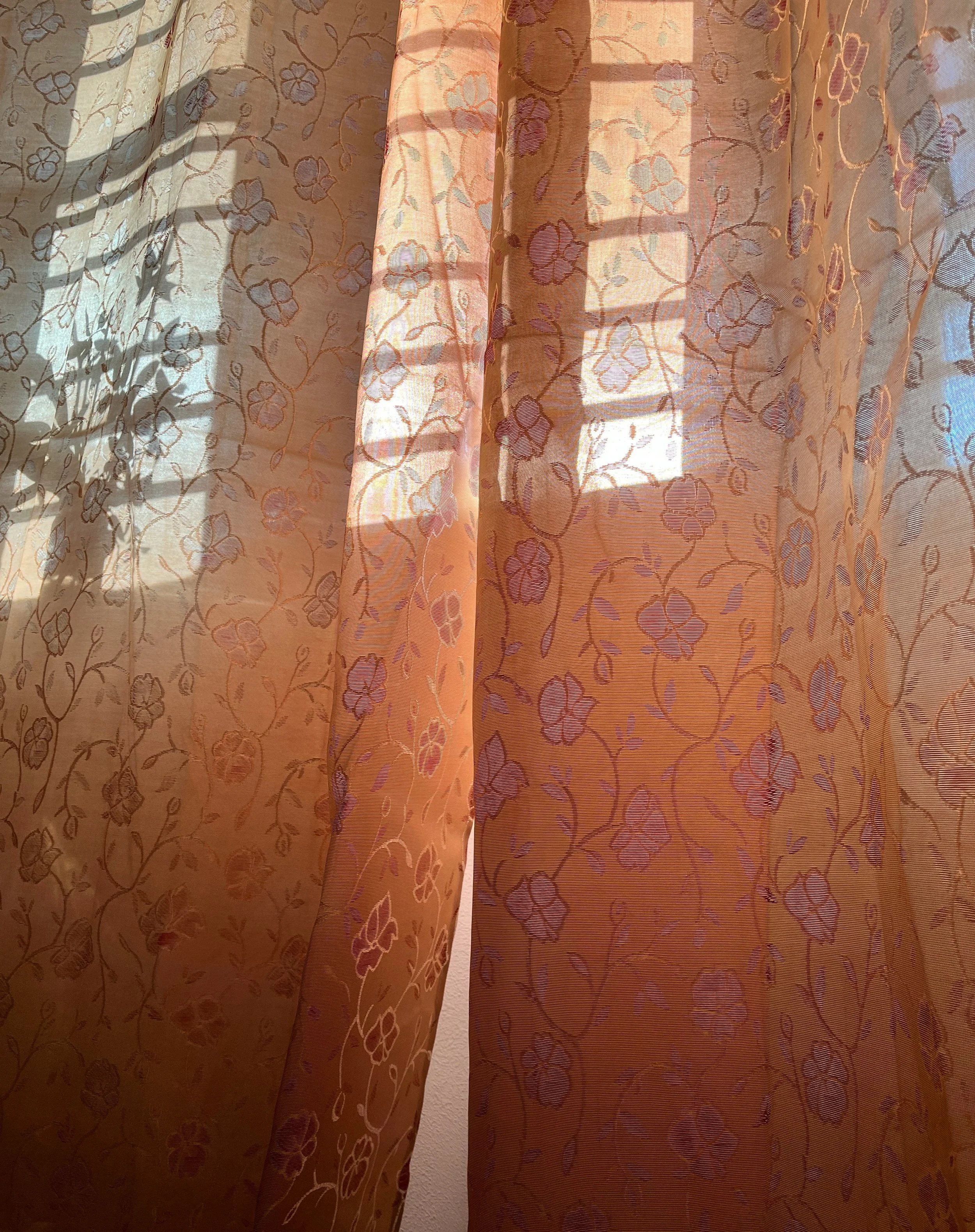 Sunlight coming through sheer floral-patterned curtains, creating shadow patterns on the fabric.