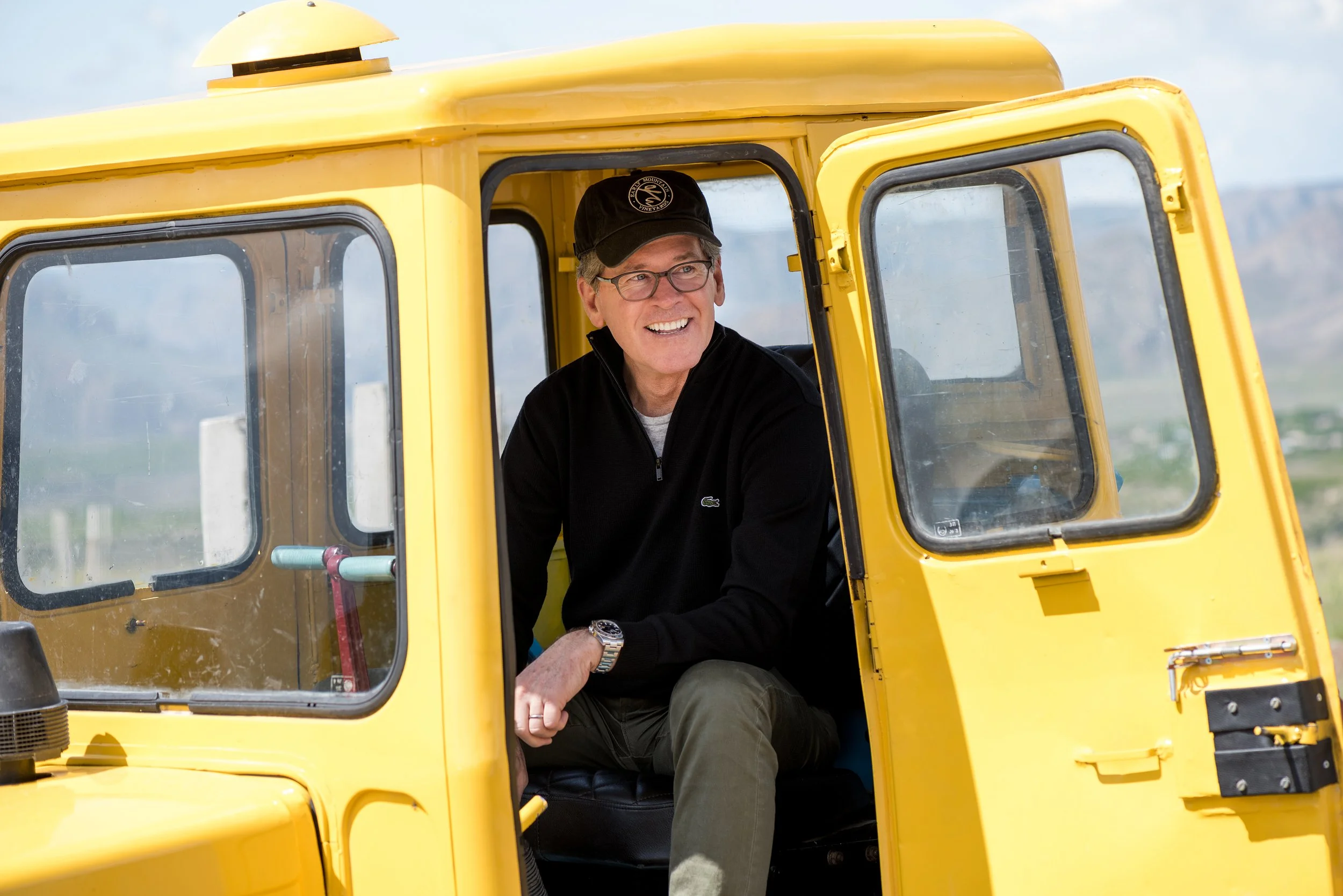 Winemaker and partner Paul Hobbs smiling while sitting in the driver's seat of a yellow vineyard tractor at the Yacoubian-Hobbs vineyard in Vayots Dzor.