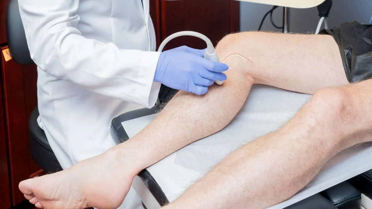 Doctor wearing blue gloves using an ultrasound probe to examine blood flow in a patient's leg