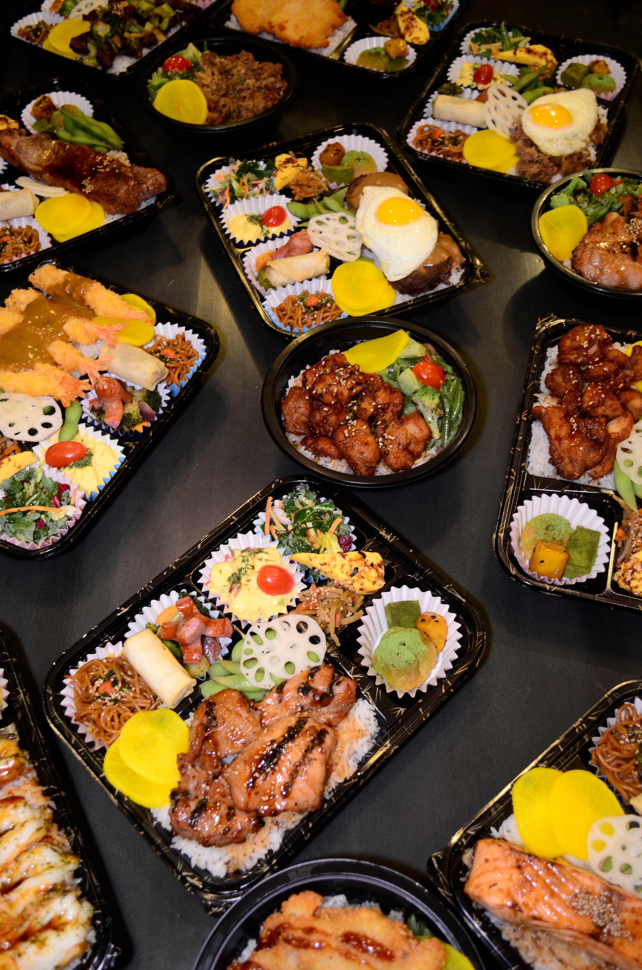 Assorted Japanese bento boxes with rice, grilled meats, fried shrimp, and vegetables.