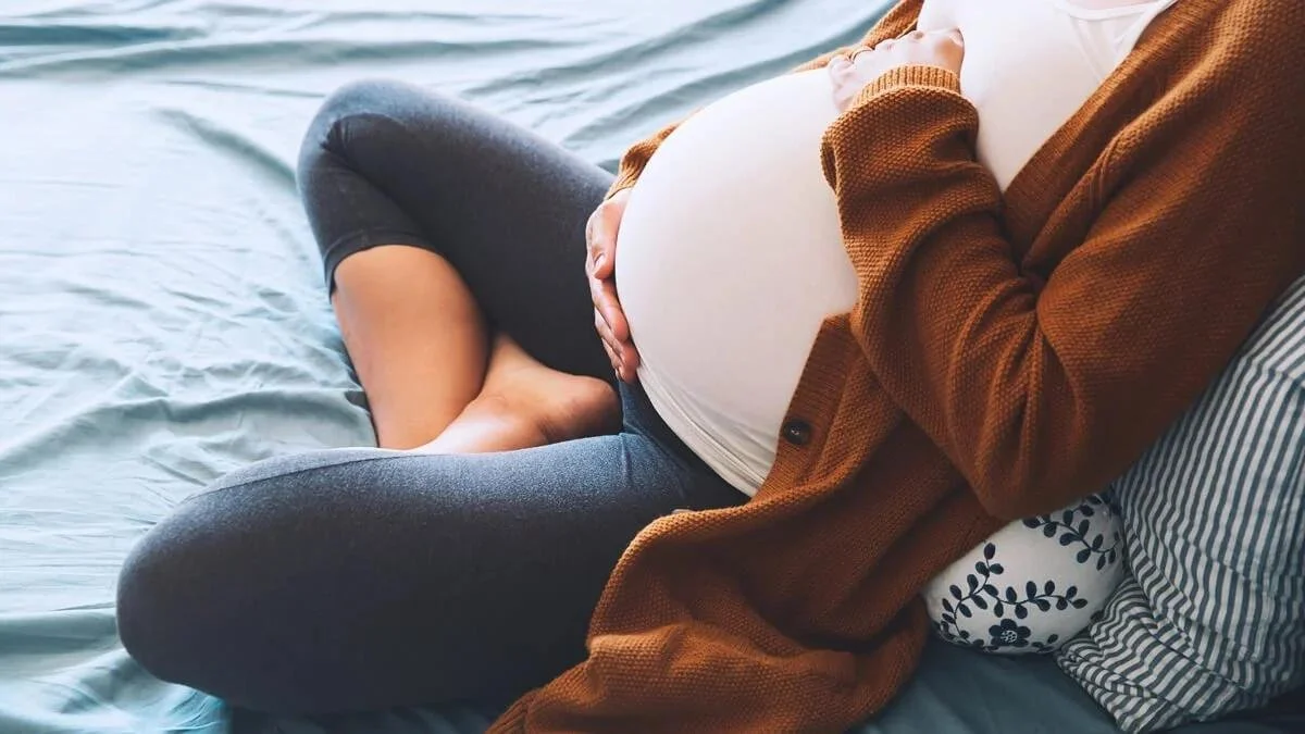 Pregnant woman resting on couch holding lower back with pelvic pain symptoms