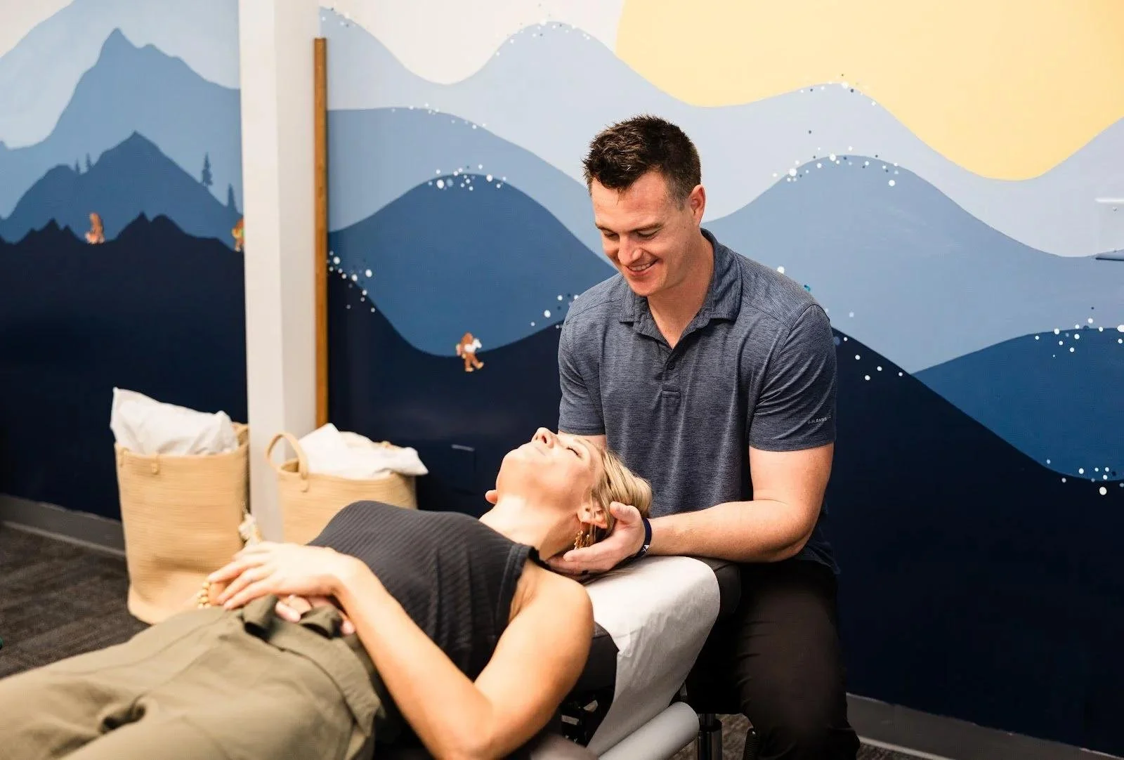Dr Garrett Smith adjusting woman in mountain mural room during sports injury care in Liberty MO