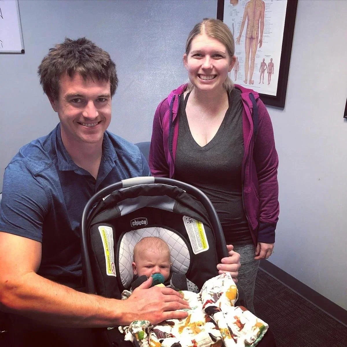 Parents smiling with infant in car seat during tongue tie chiropractic visit in Liberty MO