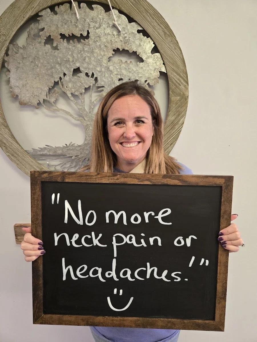 Woman holding chalkboard about no more neck pain or headaches after treatment