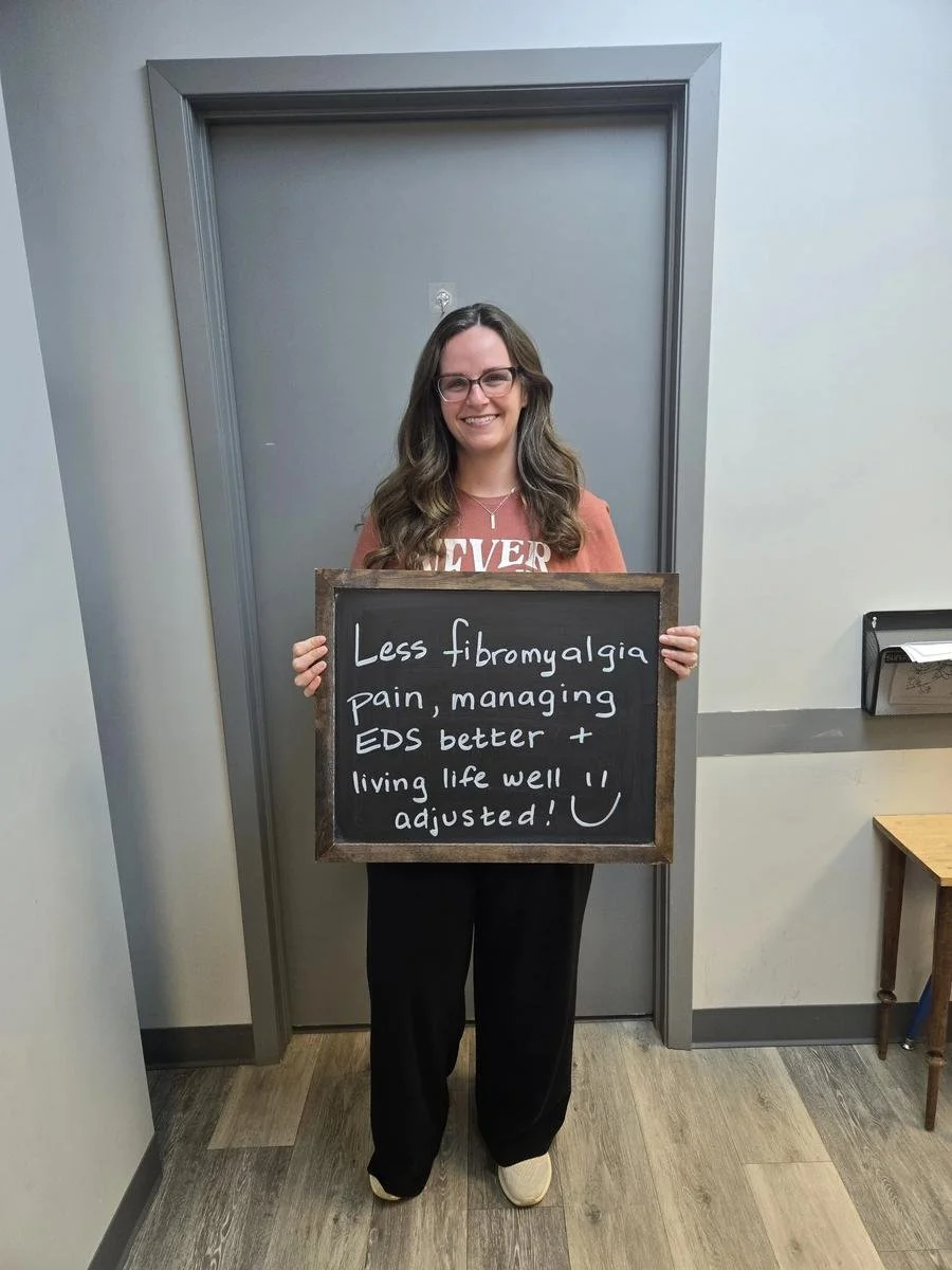 Woman holding chalkboard about less fibromyalgia and managing EDS better with nervous system care in Liberty MO