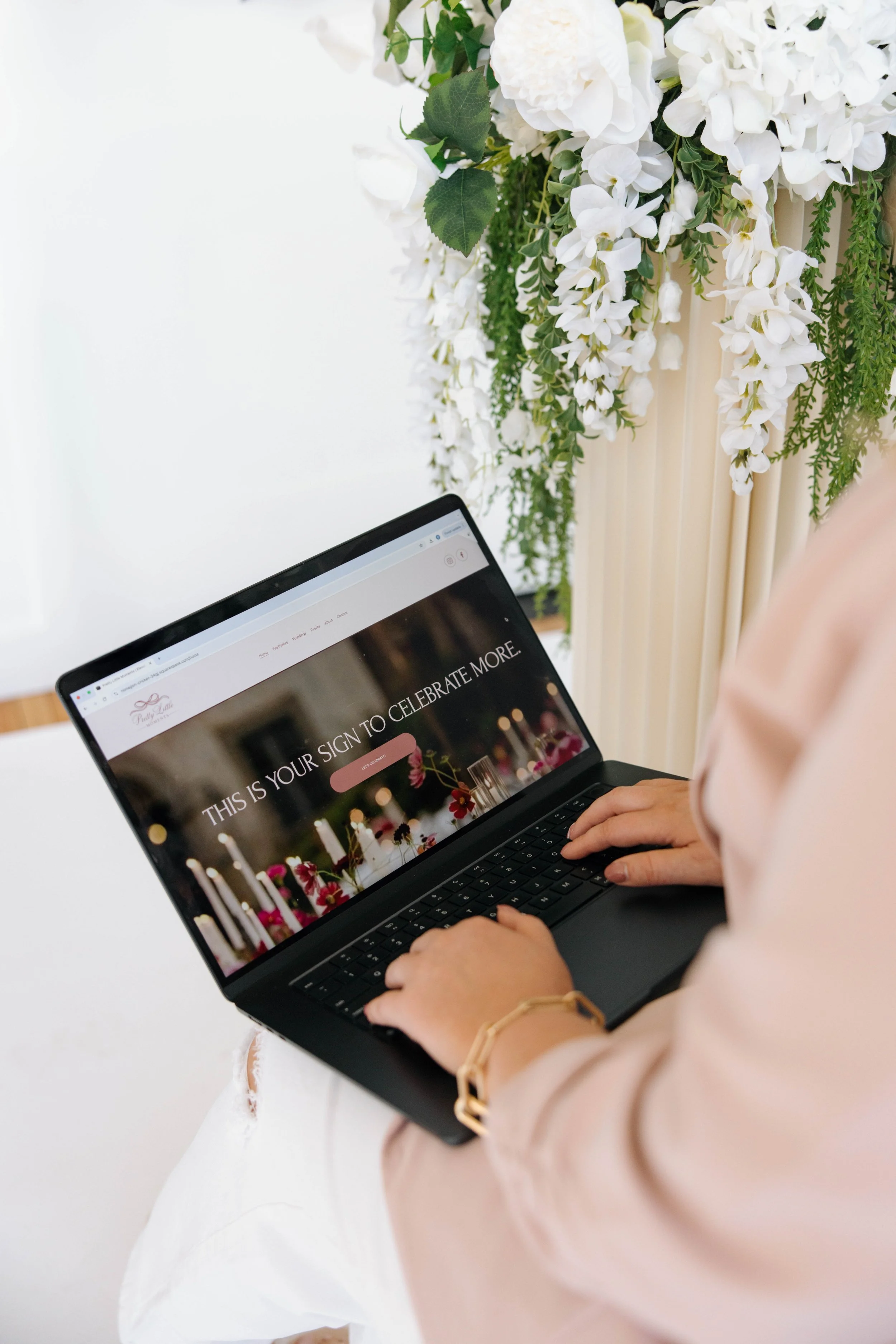 Person using a laptop, decorated with a floral arrangement of white flowers and greenery.