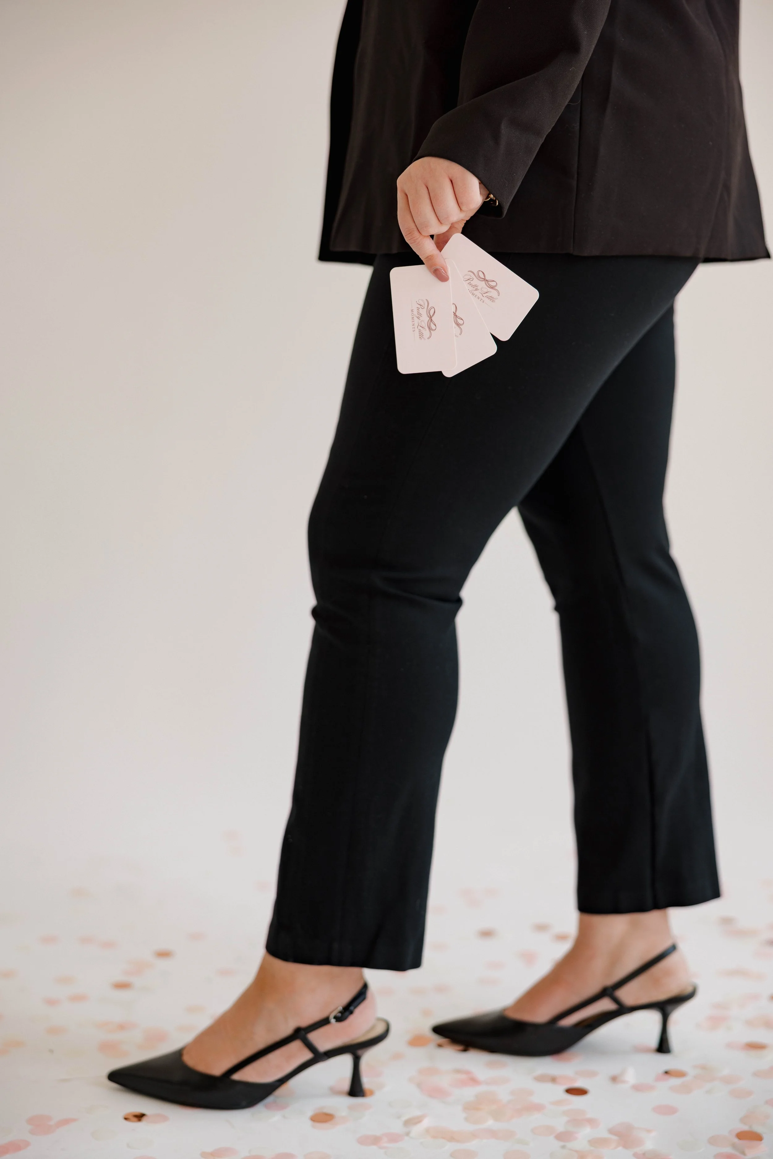 Person in black business attire holding event tickets, standing on a floor scattered with rose gold and white confetti.