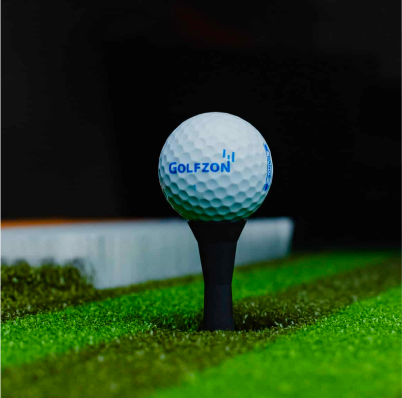 Close-up of a golf ball on a tee on a putting green, with GOLFZON on the golf ball.
