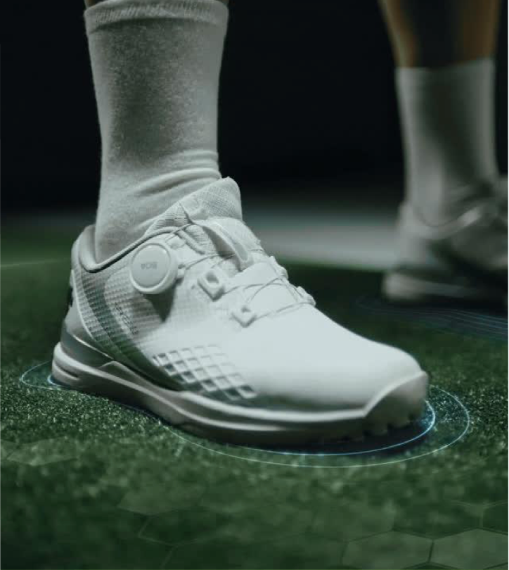 Close-up of a white athletic shoe on a green surface with a digital overlay around the heel, worn with white crew-length socks.