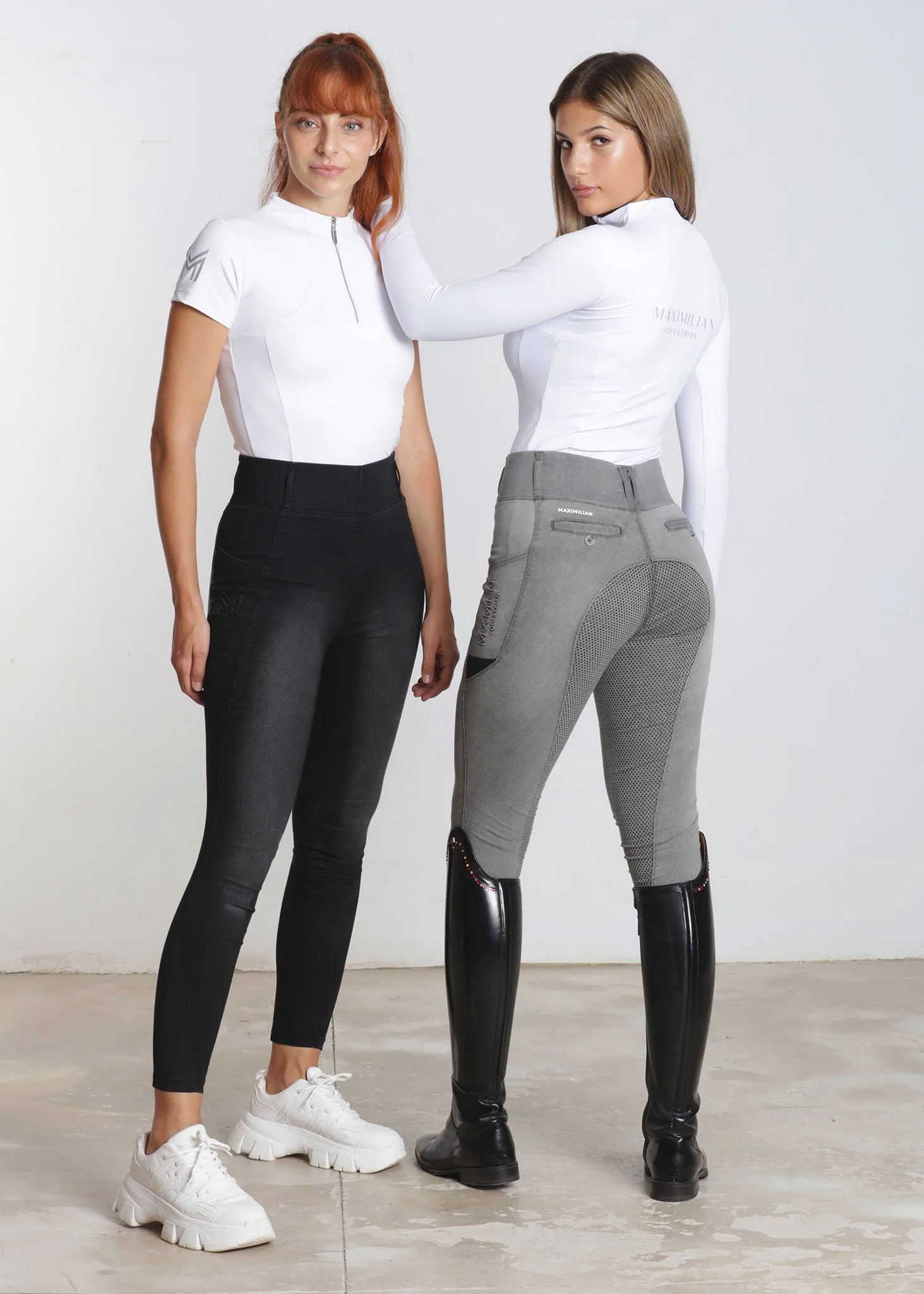 Two women wearing sporty outfits and boots. One woman facing forward with red hair and white sneakers, while the other woman, with brown hair, is turned sideways wearing black boots and gray pants.