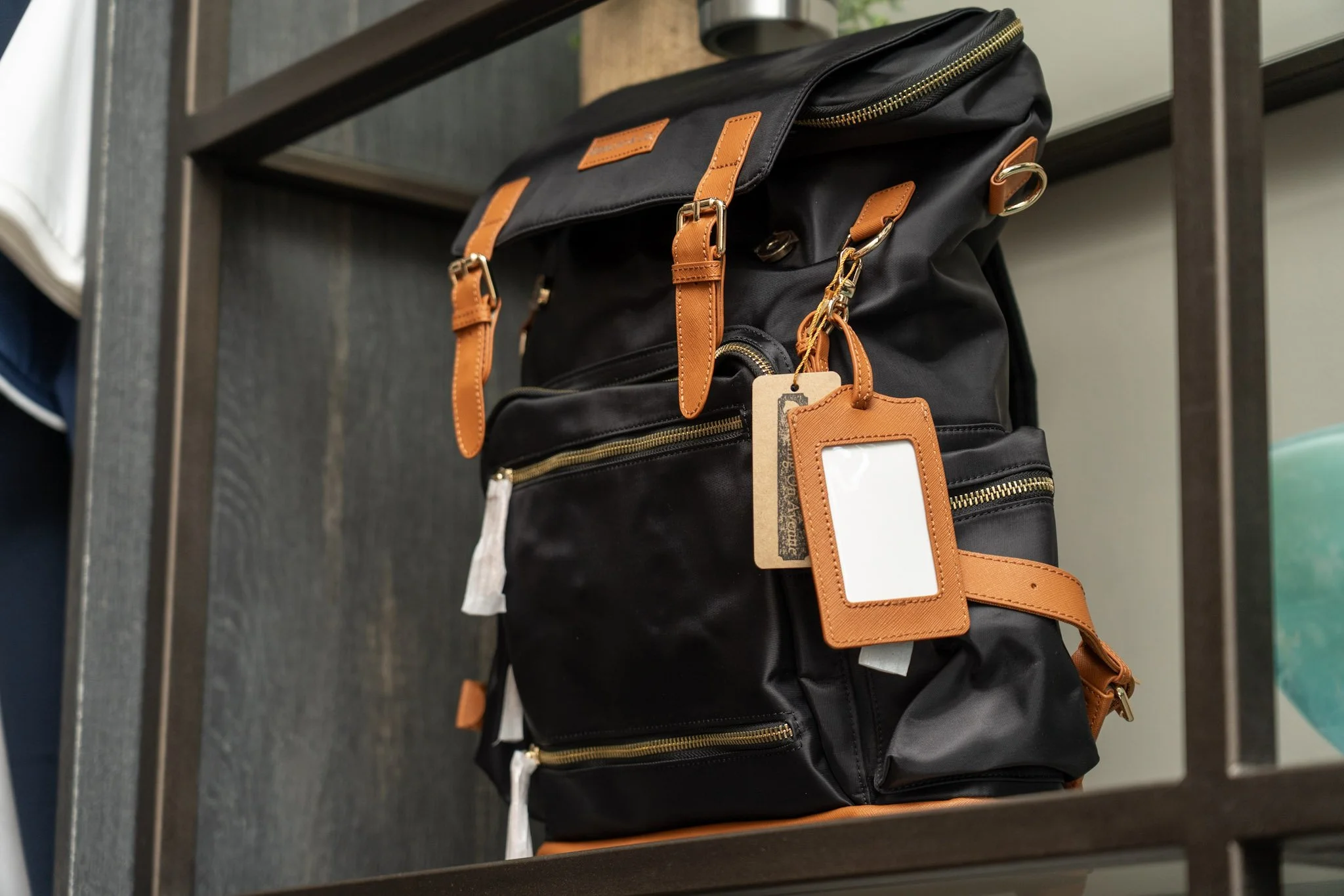 A black backpack with brown leather straps and gold zippers hanging on a metal rack.