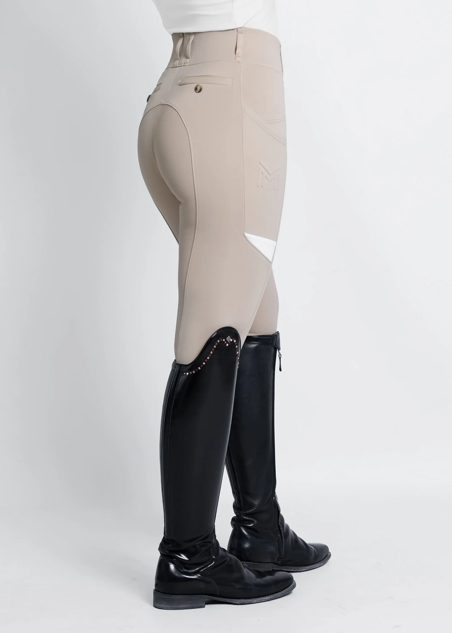 Close-up of person wearing beige riding pants and black leather riding boots, standing on a white background.