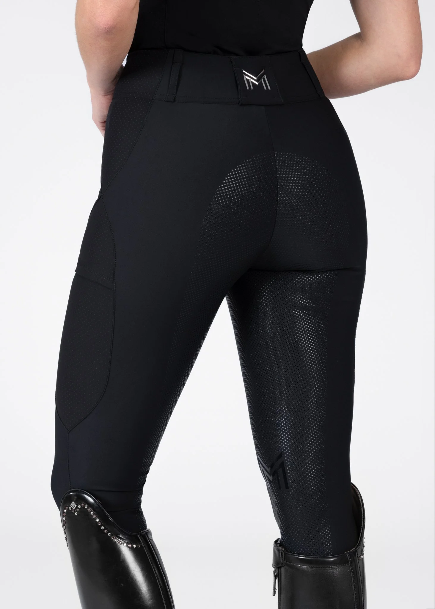 Close-up of a person wearing black athletic pants with textured panels and a logo on the waistband, paired with black knee-high boots with zipper closures.