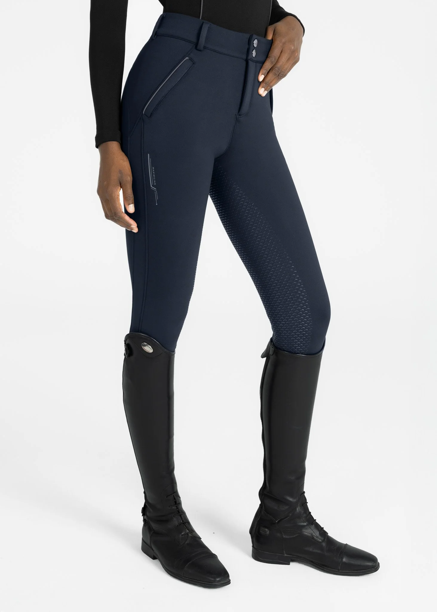 Person wearing black riding boots and navy pants with a zippered pocket on the side, standing against a white background.