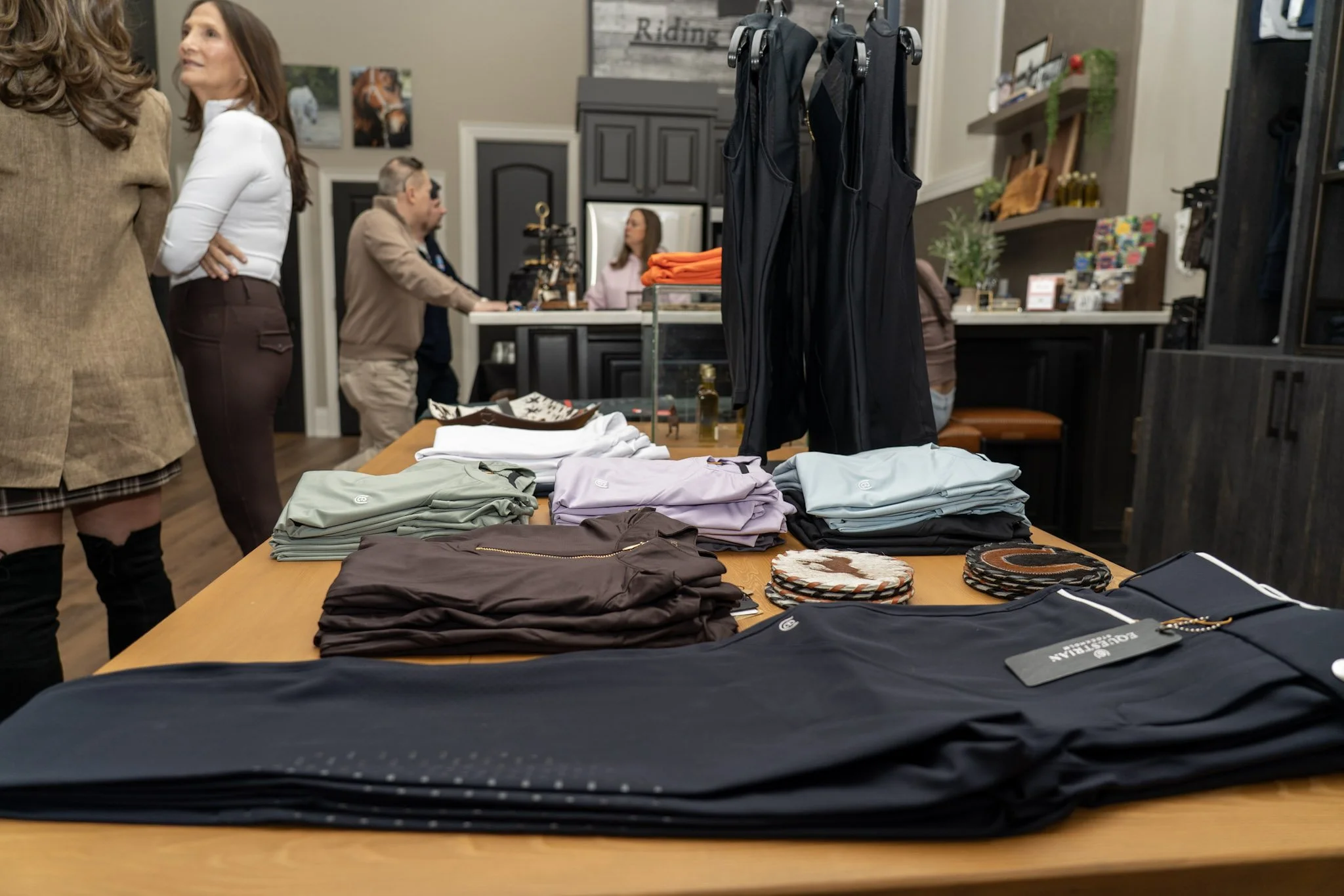 Clothing display table with folded shirts and pants in a retail store, with customers and employees in the background.