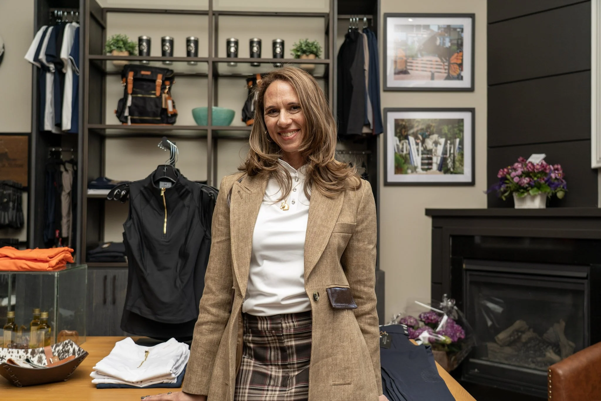 A woman with brown hair smiling in a retail store with clothing and framed pictures on the wall in the background.