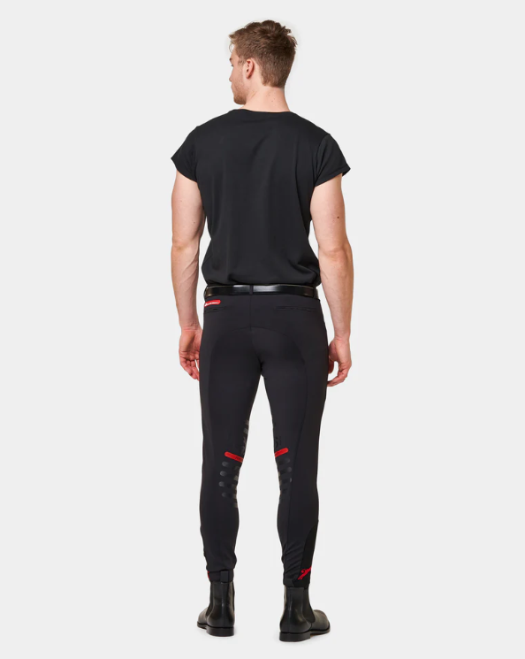 Man wearing a black t-shirt, black pants with red accents, and black boots, standing with his back facing the camera against a plain gray background.