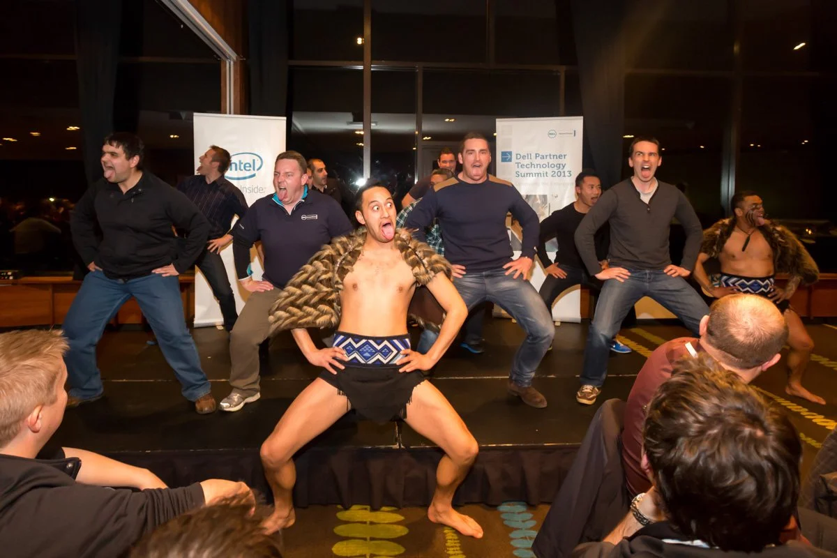 Group of men performing a dance on stage at a corporate event, with audience members watching.