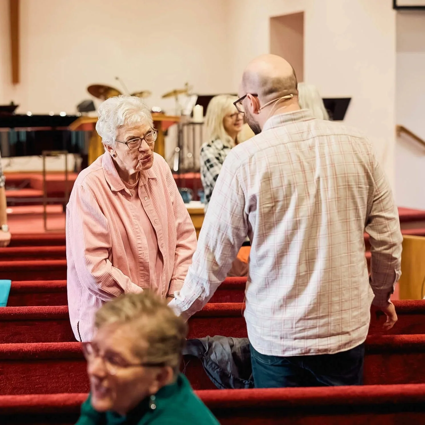 Viewed from behind, the Crown Hill Church pastor stands in the pews in warm conversation with an older woman during community time in the service.