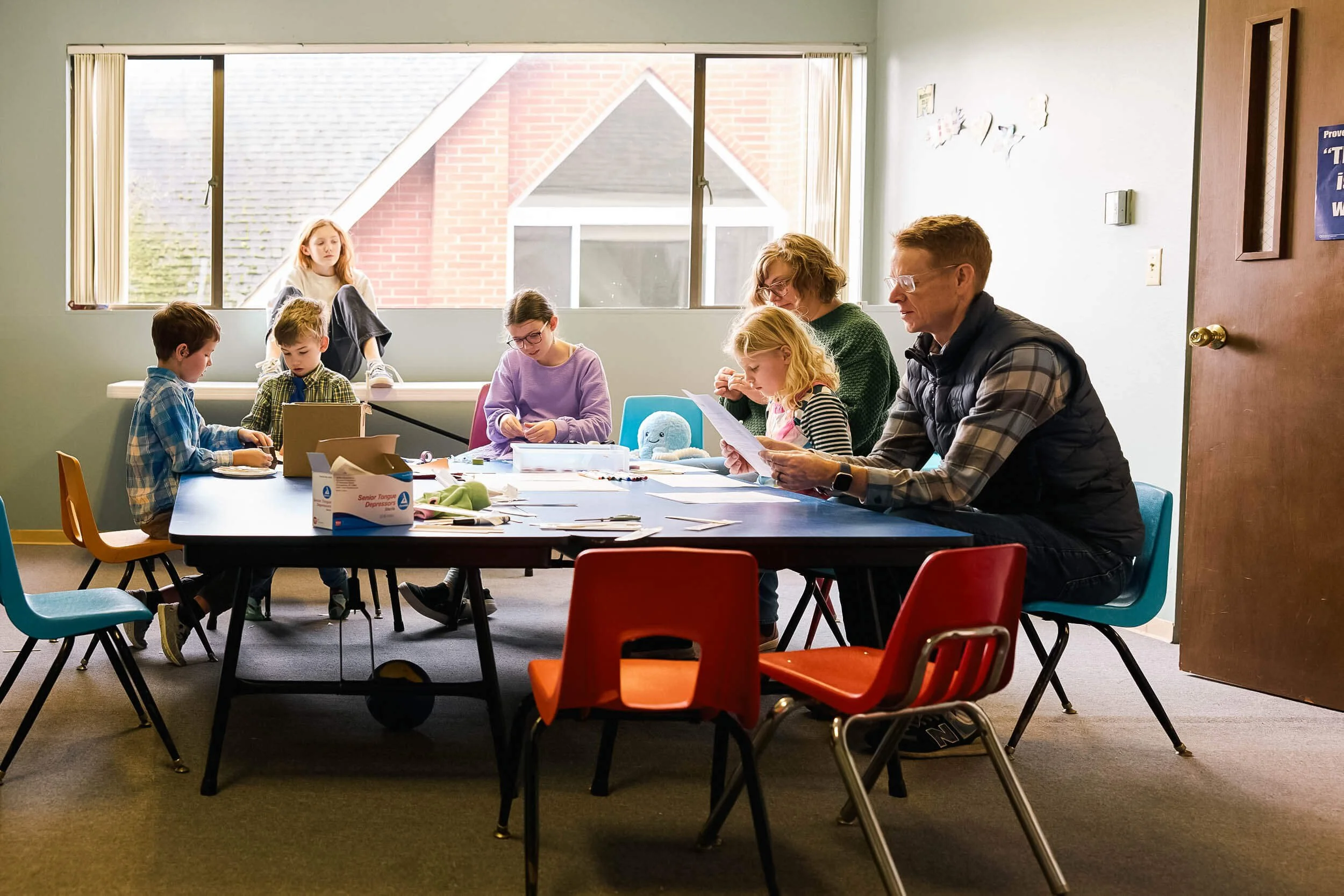 Five elementary and middle school aged children sit at a table with the Crown Hill Church youth pastor and a volunteer, happily engaged in crafts together during Sunday school.