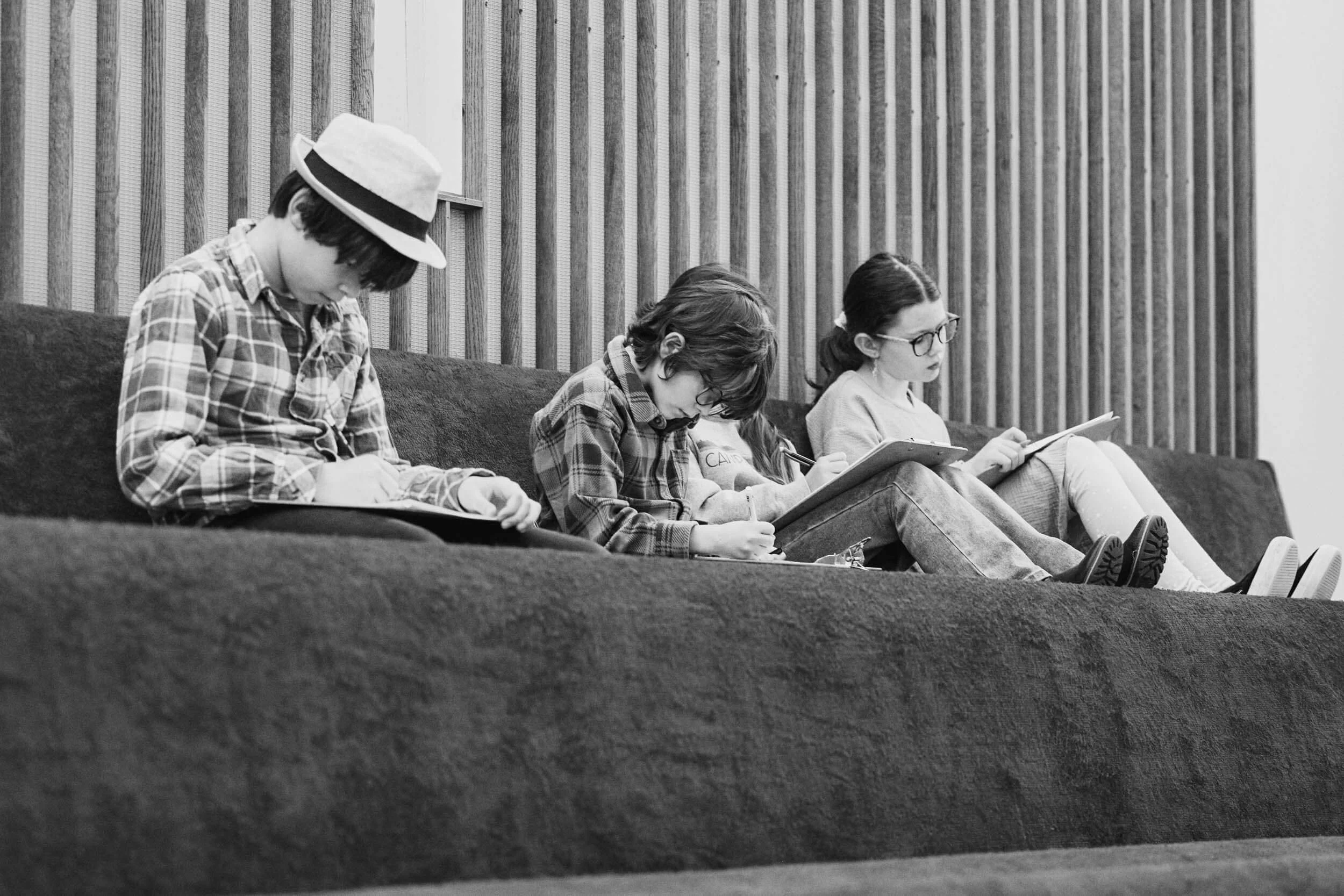 A black and white image of four youth sitting together in the balcony pews, each drawing and quietly focused during the worship service at Crown Hill Church.