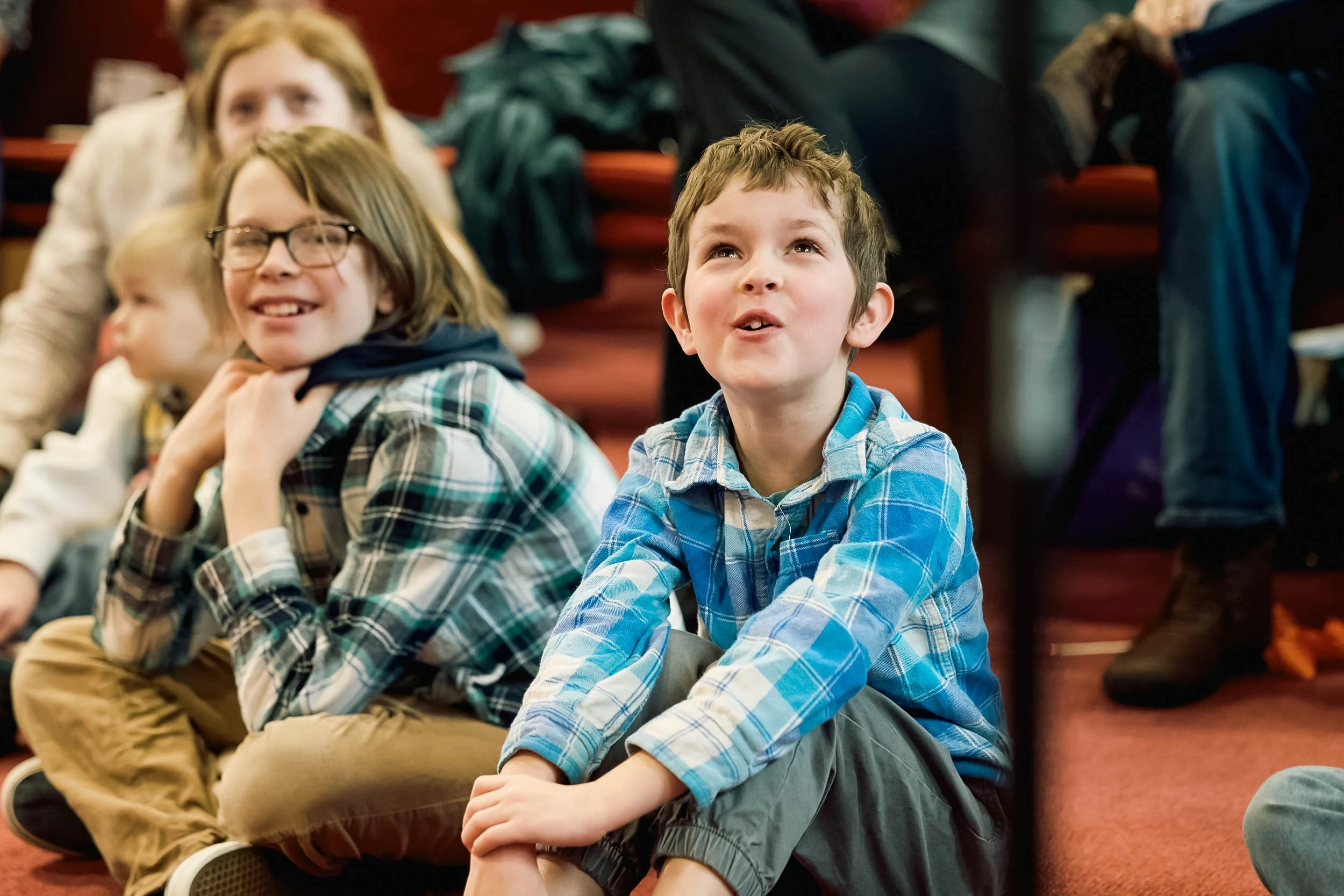 A close up of several children sitting on the floor with big smiles during the Kids Moment at Crown Hill Church, where children are welcome in the worship service.