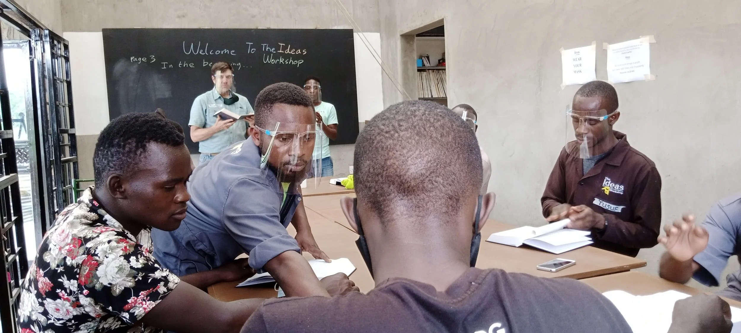 Four men read text together as one points to a passage during an Ideas Workshop training session in Uganda, a ministry partnership supported by Crown Hill Church.