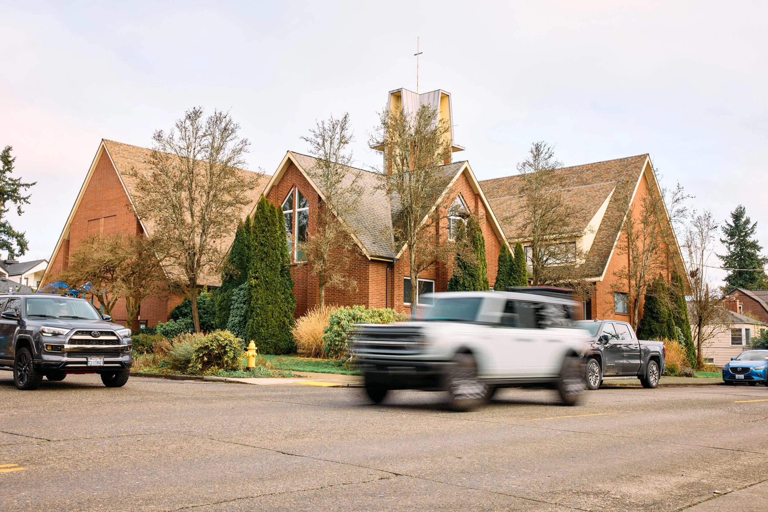 The exterior of Crown Hill Church at the corner of NW 80th and Mary Avenue in Seattle's Crown Hill neighborhood, with a car waiting at a stop sign and another passing in the foreground.