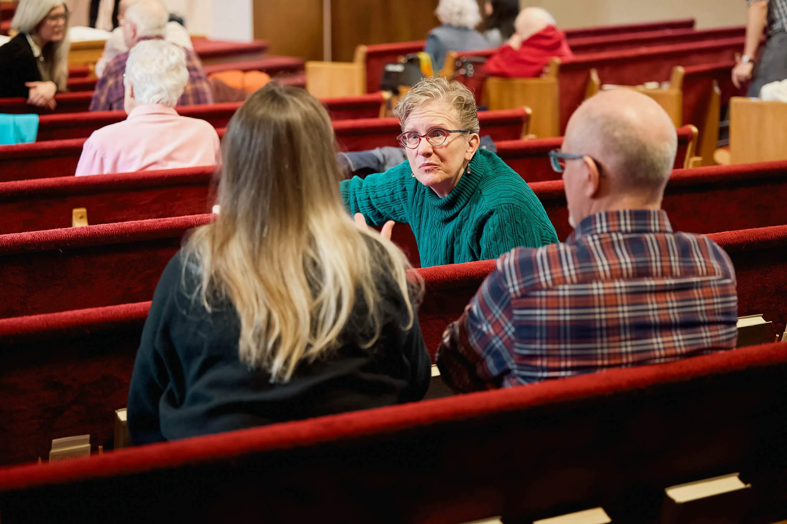 Two women and a man turn toward one another in the pews, engaged in warm conversation before the Sunday service begins at Crown Hill Church.