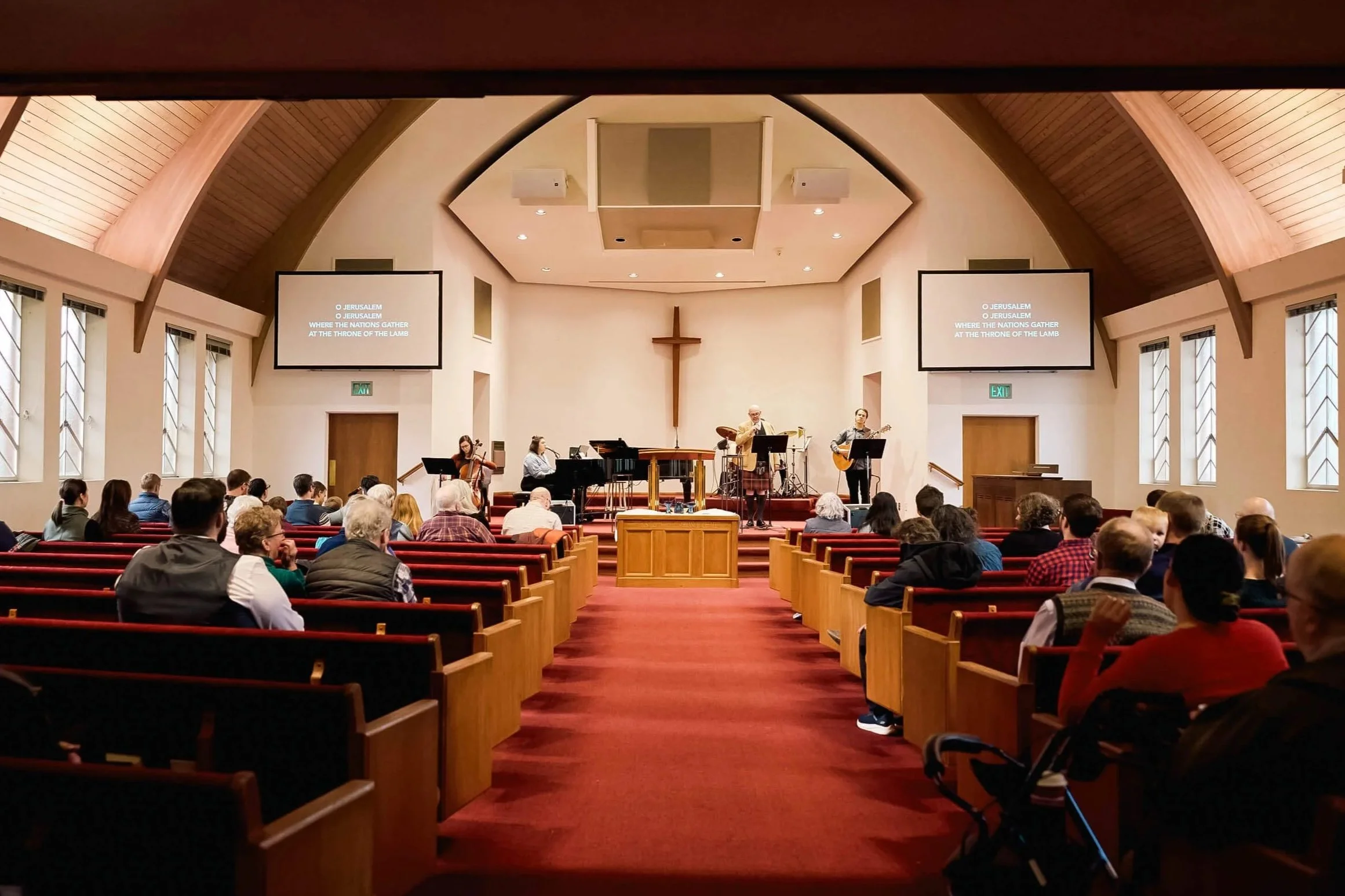 A Sunday worship service at Crown Hill Church in Seattle, featuring a live band leading music from the front while the congregation participates in singing together.