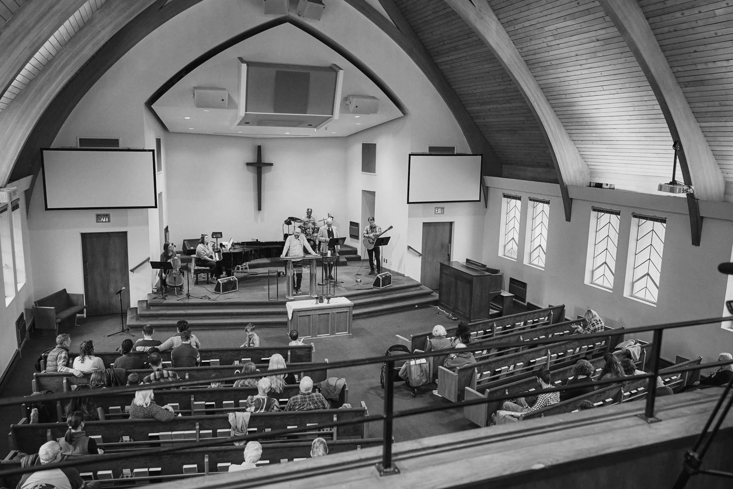 A wide shot of the Crown Hill Church sanctuary during a Sunday worship service, with the pastor speaking and the worship band on stage in Seattle's Crown Hill neighborhood.