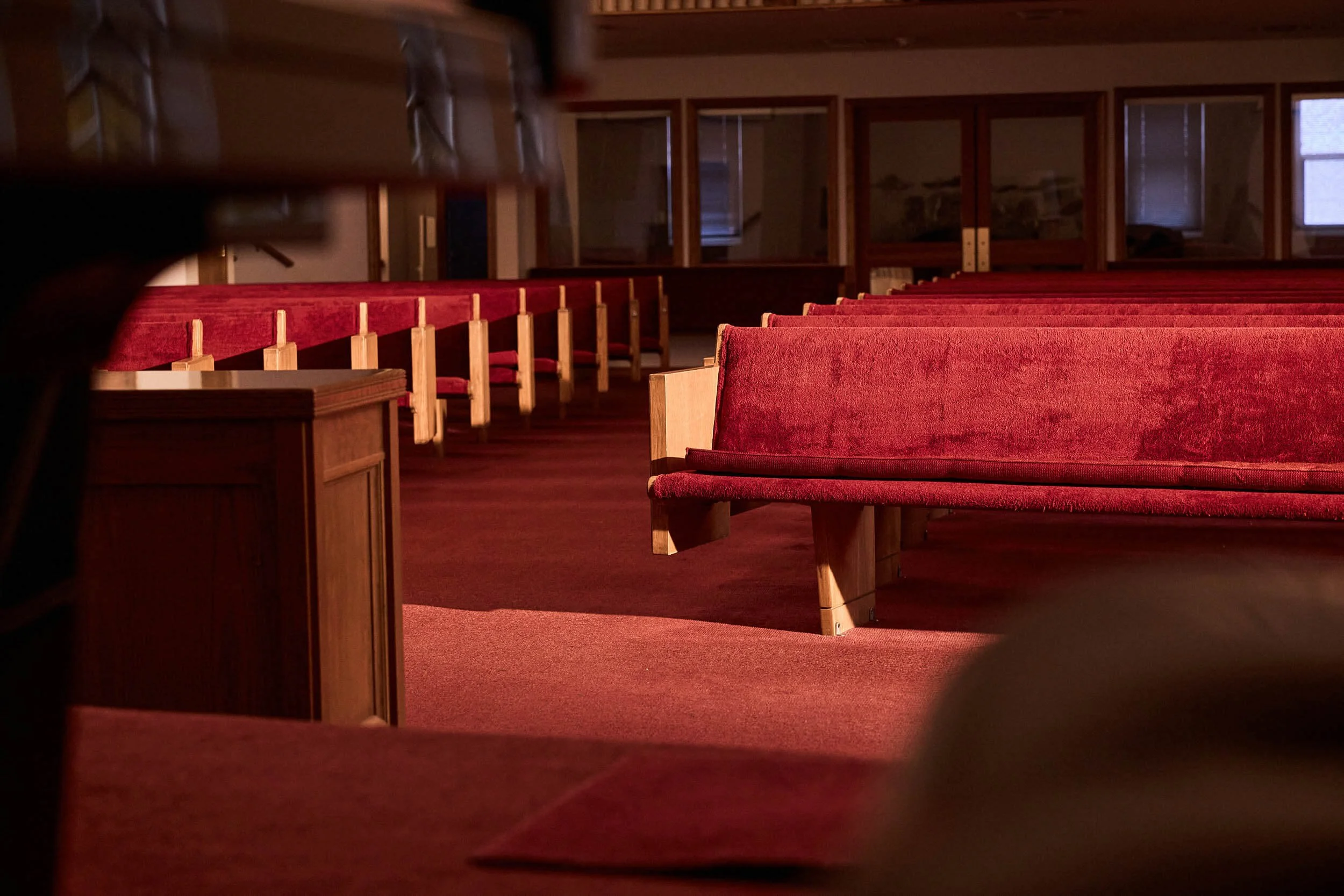 Empty church sanctuary with warm wood pews, red velvet cushions, and red carpeting at Crown Hill Church in Seattle, Washington.