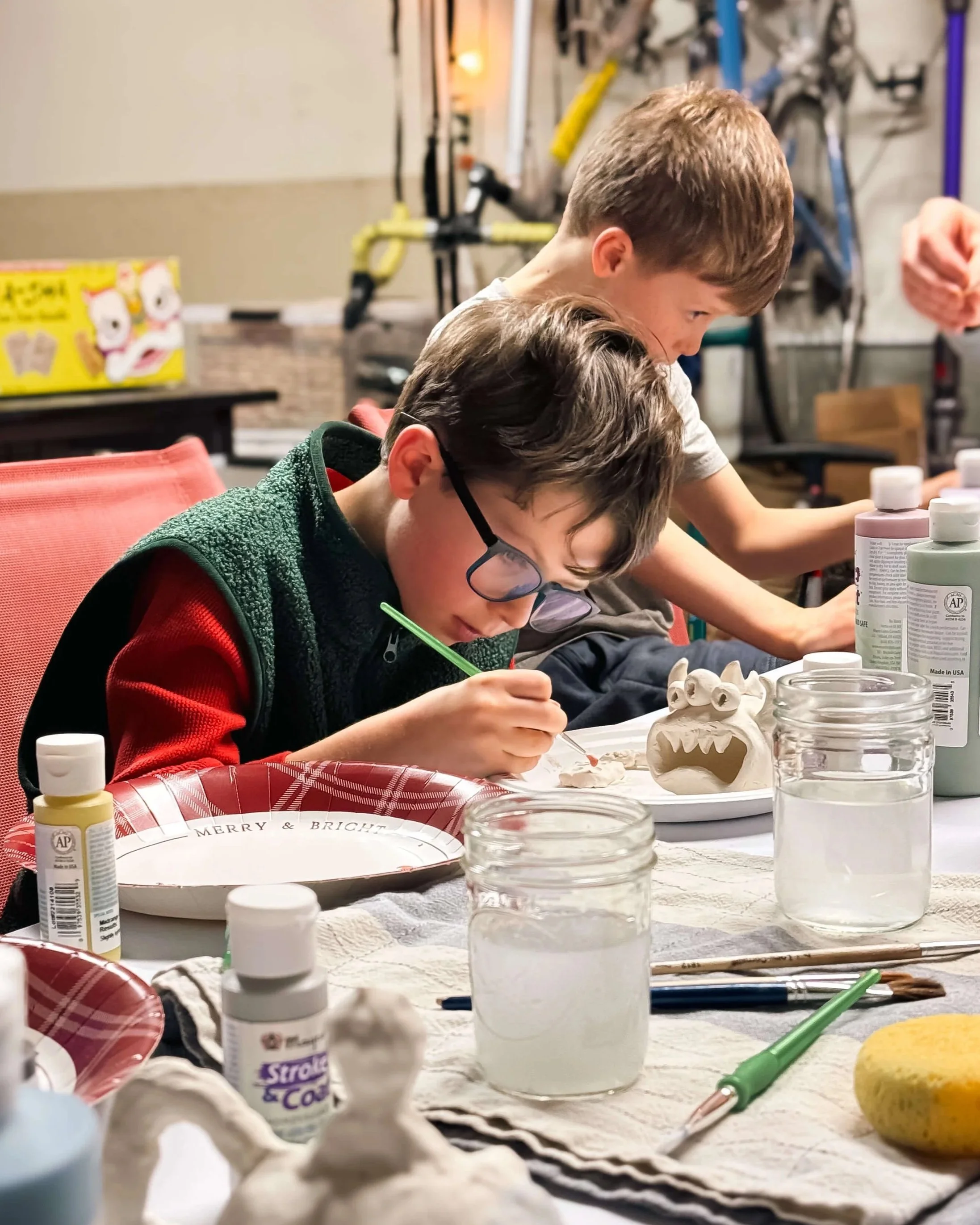Two boys sculpt and paint clay monsters together during Curious Minds Club, a Crown Hill Church community event where adults and children collaborate on creative projects in Seattle's Crown Hill neighborhood.
