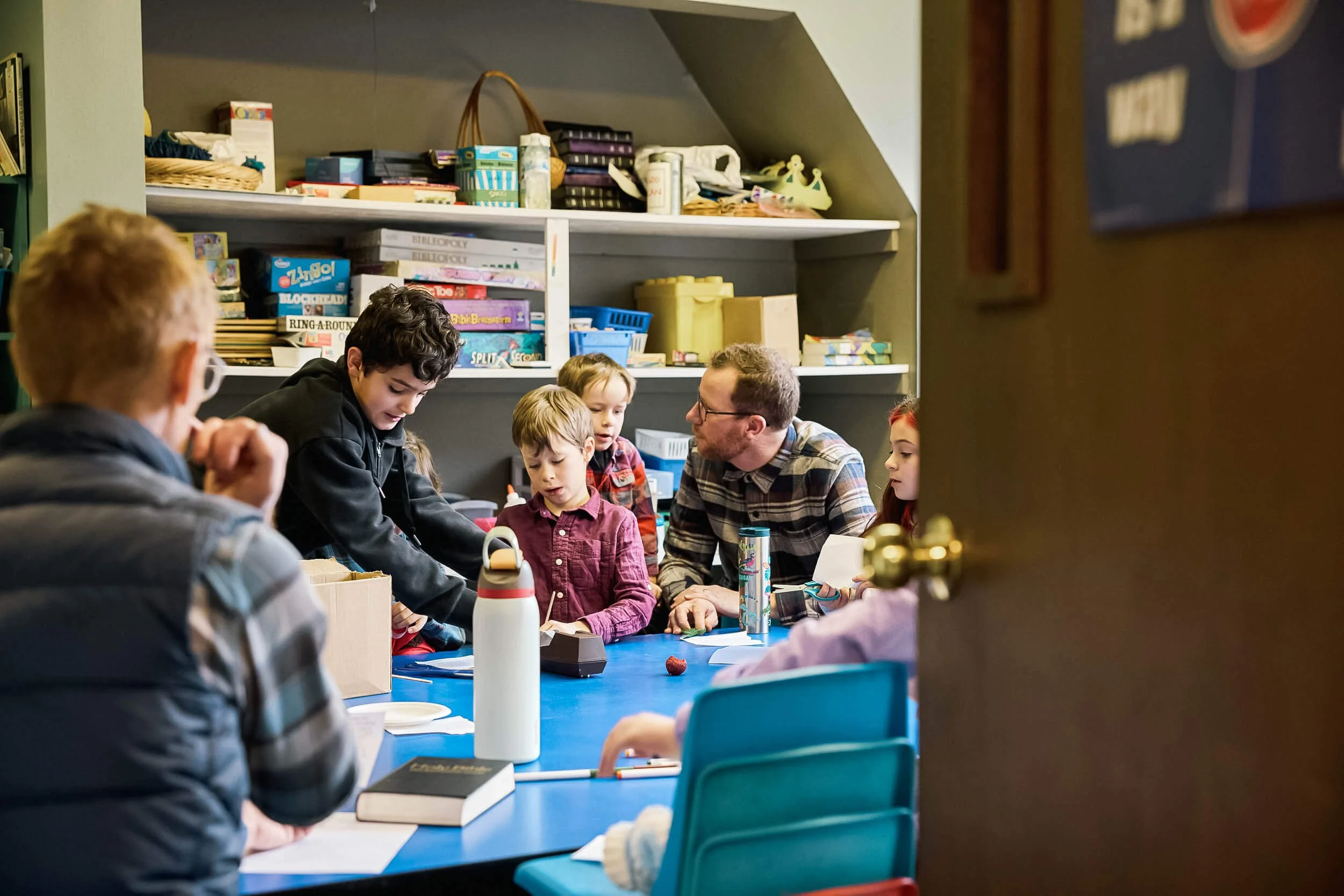 A group of elementary aged children work on an activity together while a teacher engages one on one with a student during Sunday school at Crown Hill Church.