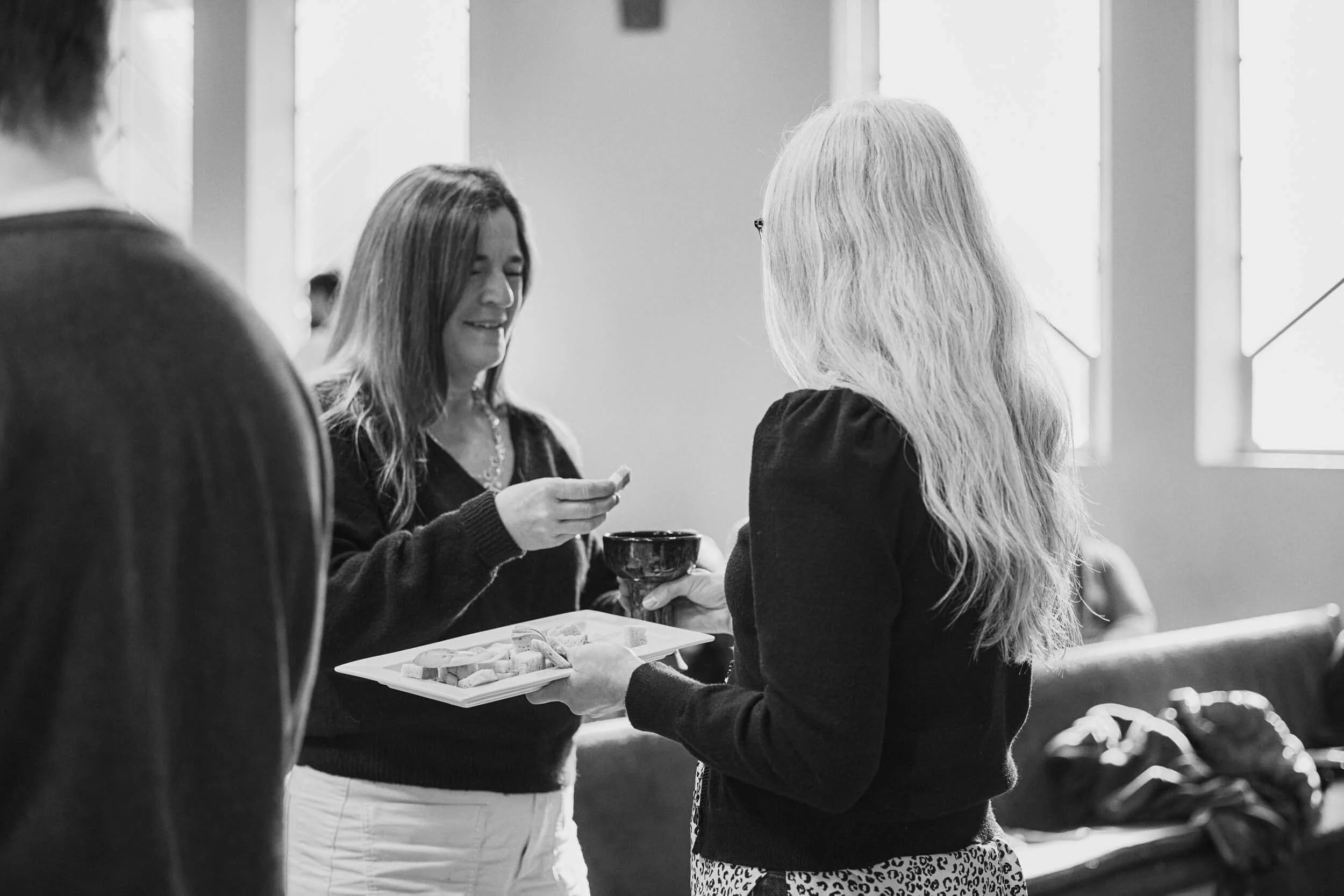 A black and white image of a woman receiving communion by intinction, dipping bread into a goblet of wine, during a worship service at Crown Hill Church in Seattle's Crown Hill neighborhood.