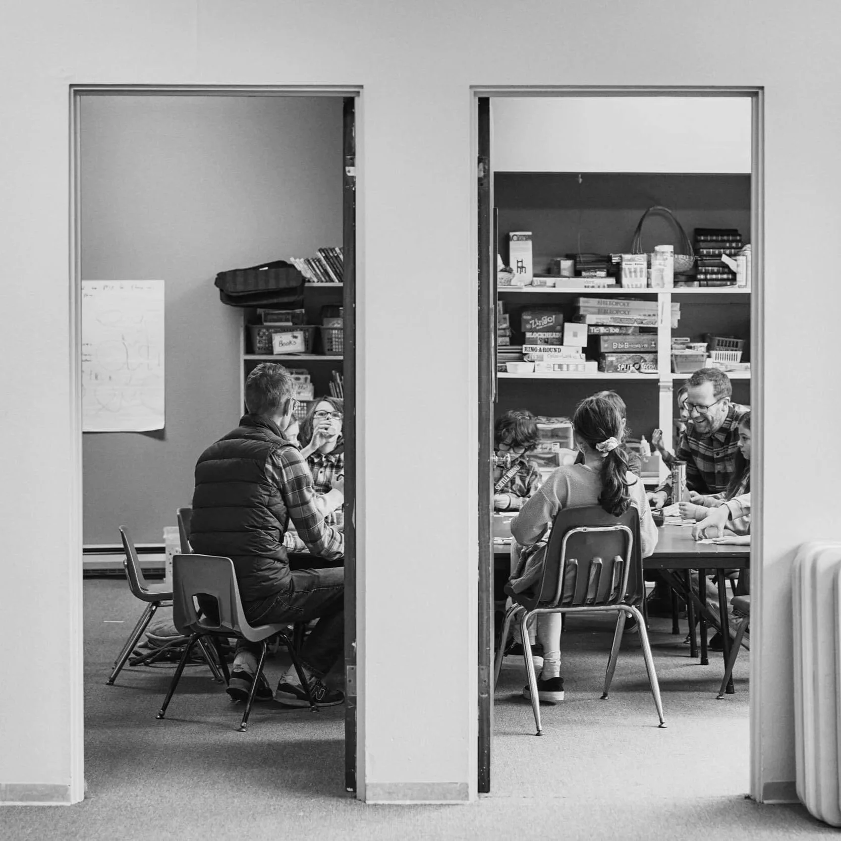 Viewed through two open doorways, adult leaders engage with a table full of elementary and middle school aged children during Sunday school at Crown Hill Church.