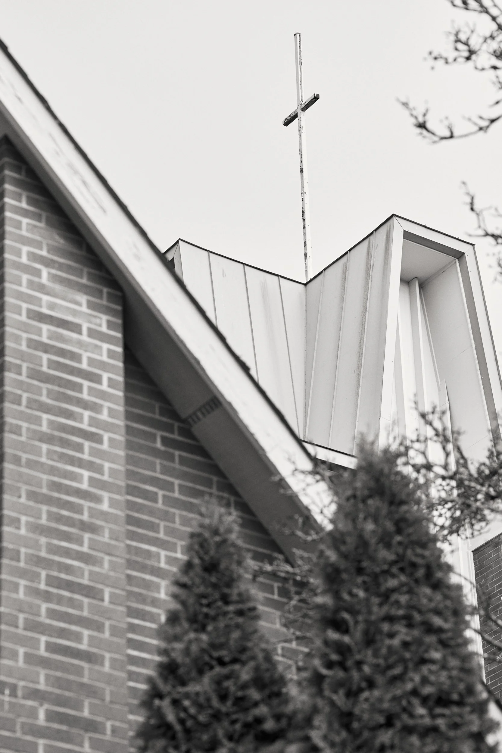 A black and white upward view of the brick exterior of Crown Hill Church, with the thin cross and steeple rising against the sky in Seattle's Crown Hill neighborhood
