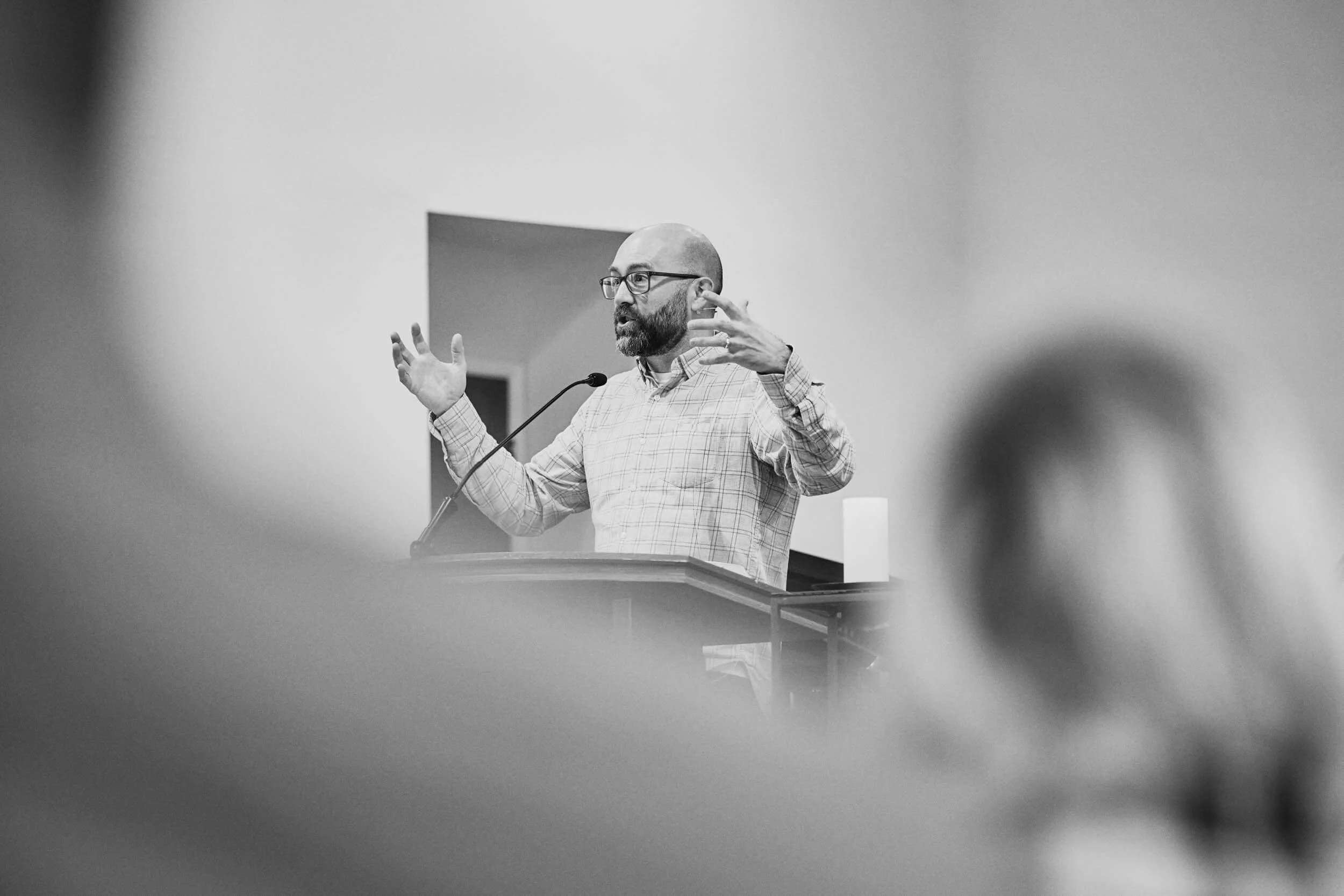 A black and white image of the Crown Hill Church pastor preaching with both hands raised in an expressive gesture during a Sunday sermon.