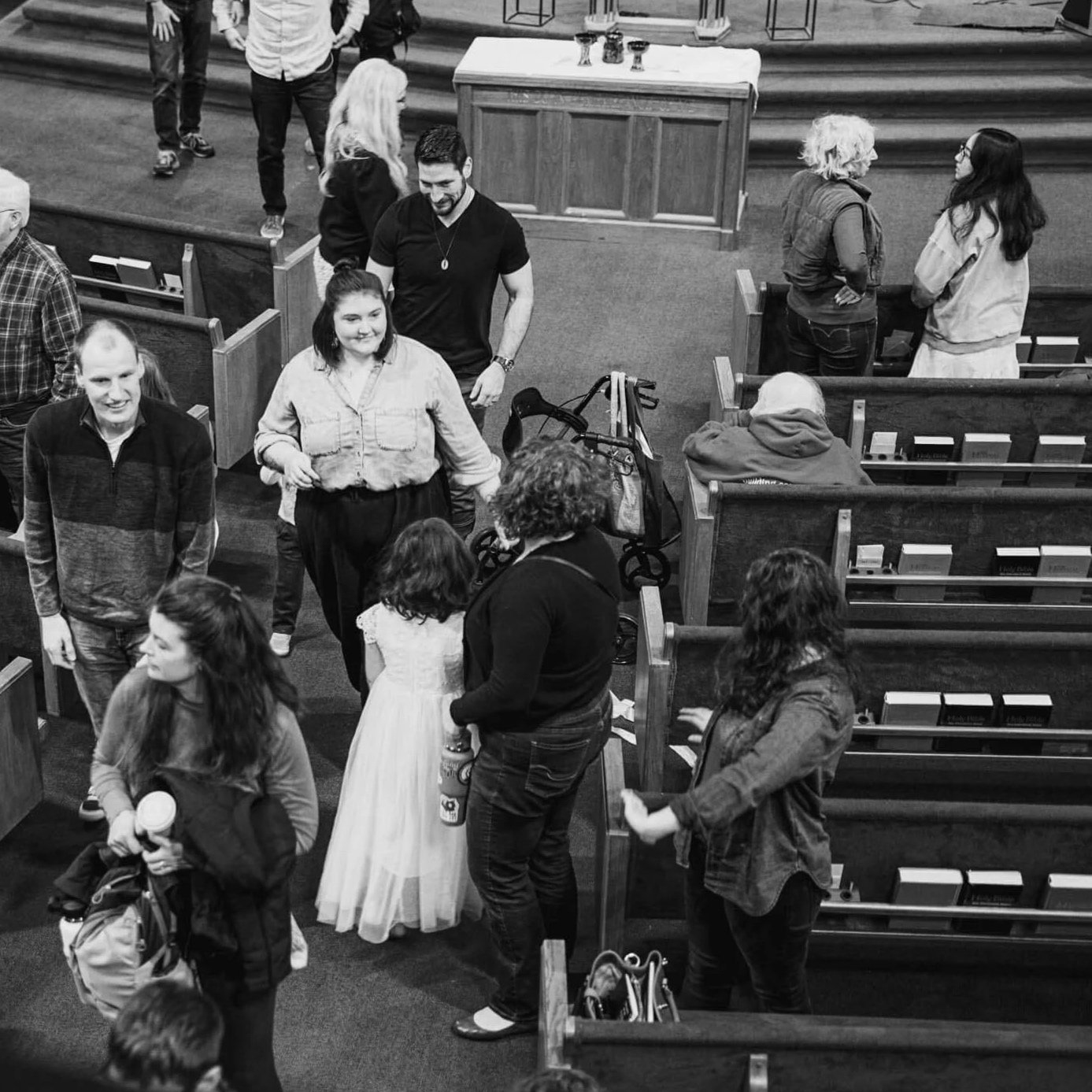 A black and white image of Crown Hill Church congregation members moving about and warmly greeting one another at the close of a Sunday service.